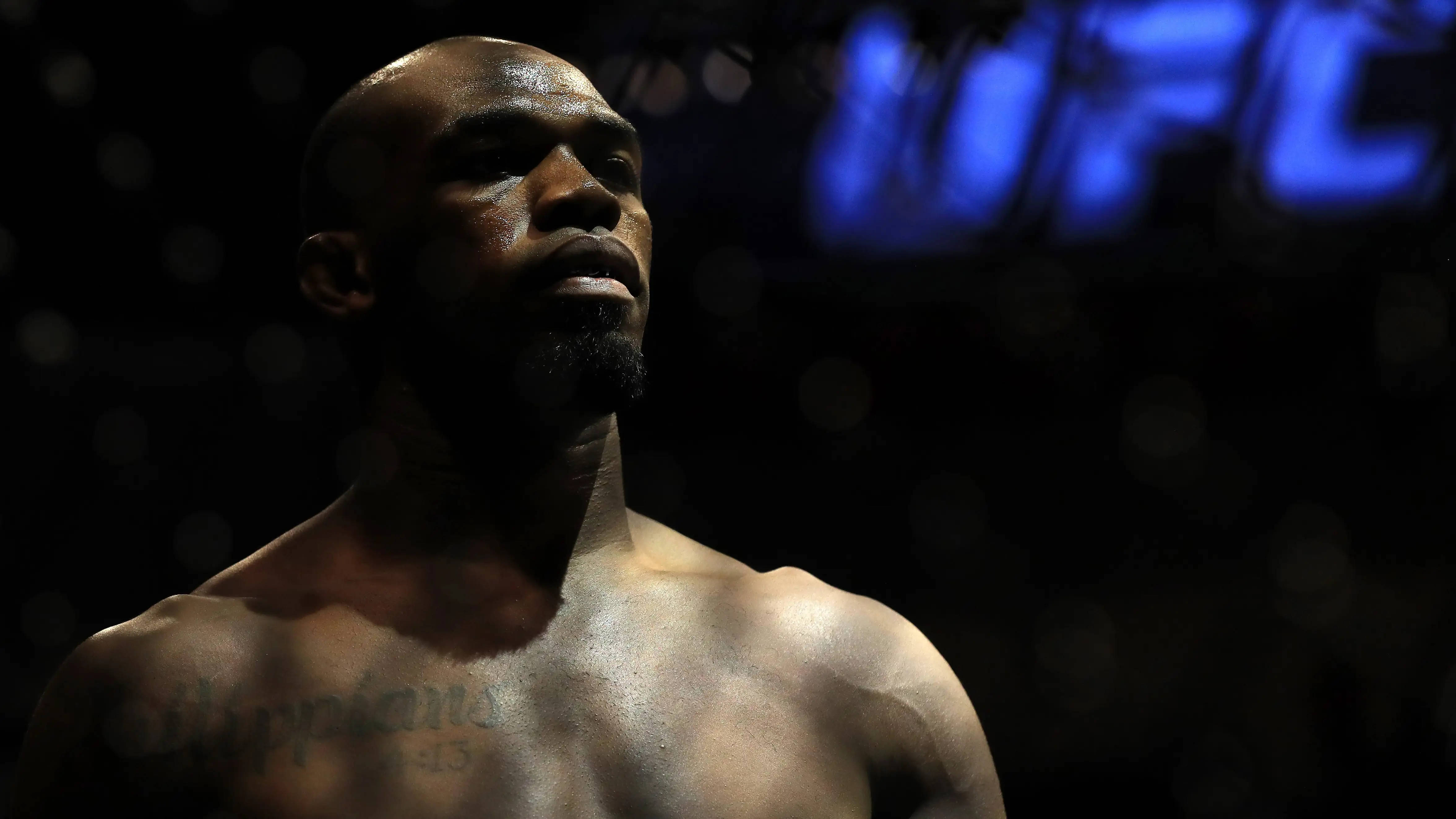UFC 桌布 壁紙 — 一位專注的UFC拳手在八角籠內，在戲劇性的藍色燈光下向上凝視，背景有模糊的標誌。