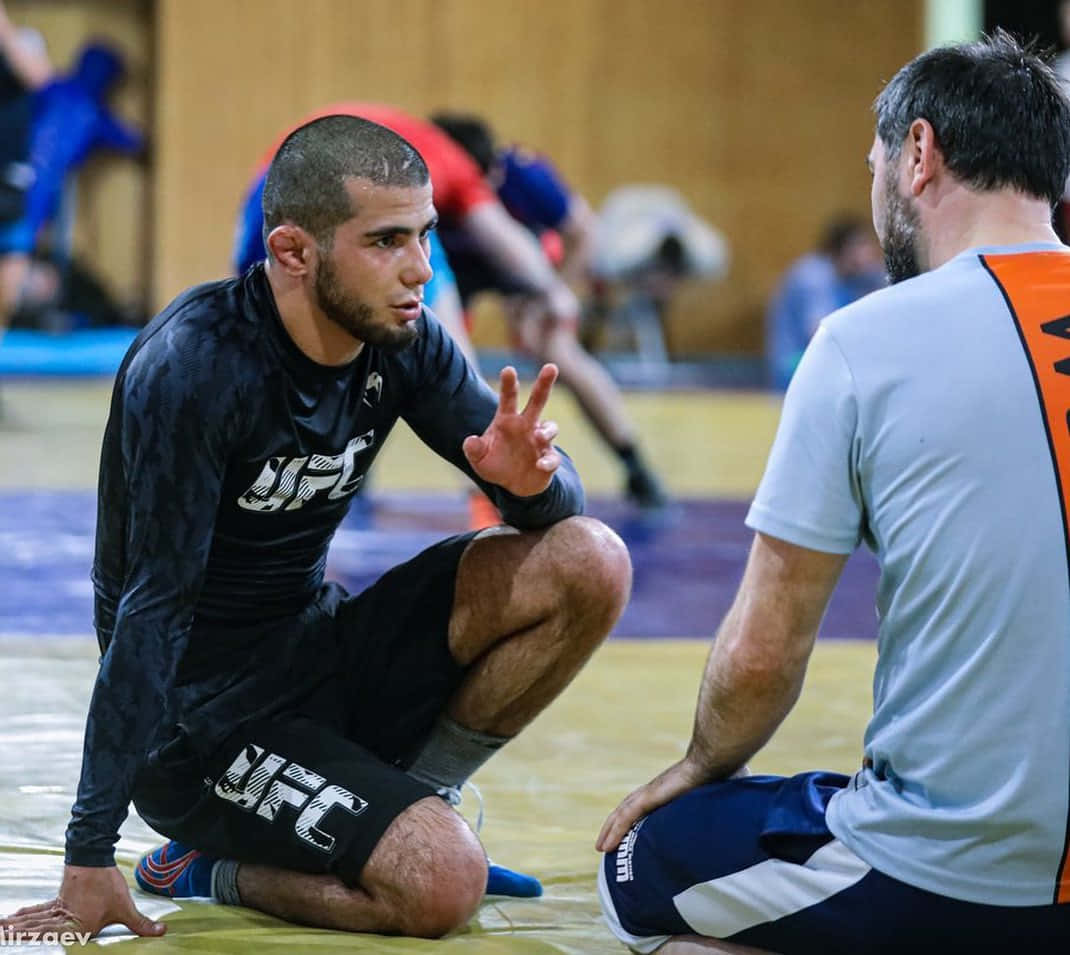 UFC 桌布 壁紙 — 一位專注的UFC拳手跪在墊子上，在訓練期間與教練激烈討論策略。
