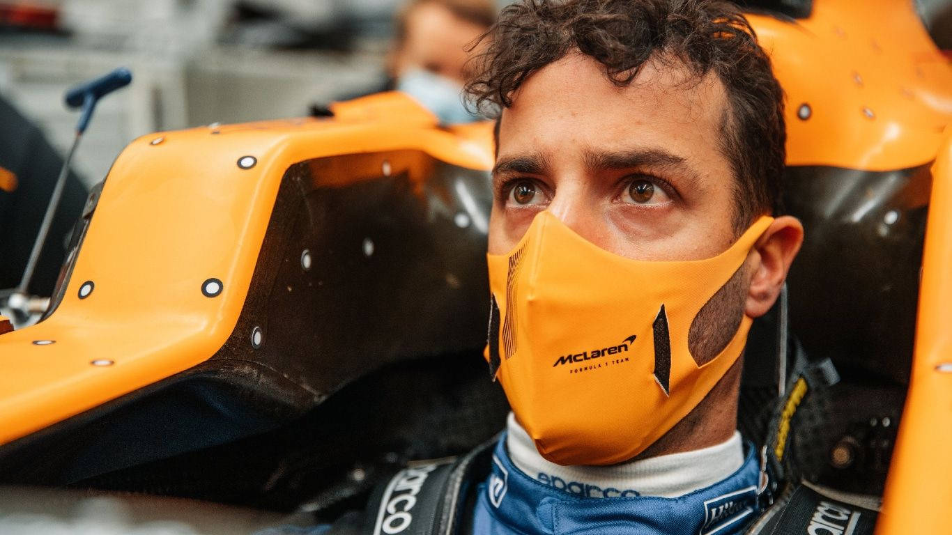 F1 桌布 壁紙 — 一位專注的一級方程式車手，戴著橙色McLaren頭盔和口罩，坐在賽車駕駛艙內。