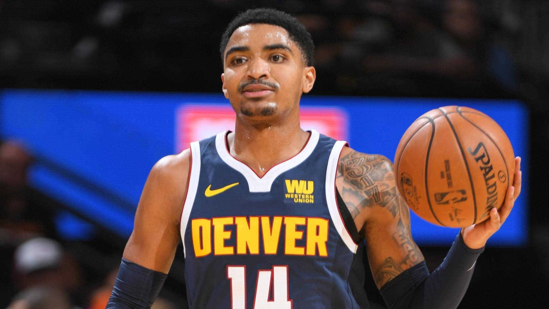 gary harris 桌布 壁紙 — 一位專注的丹佛金塊籃球運動員身穿海軍藍球衣，在場館燈光下拿著一個Spalding籃球。