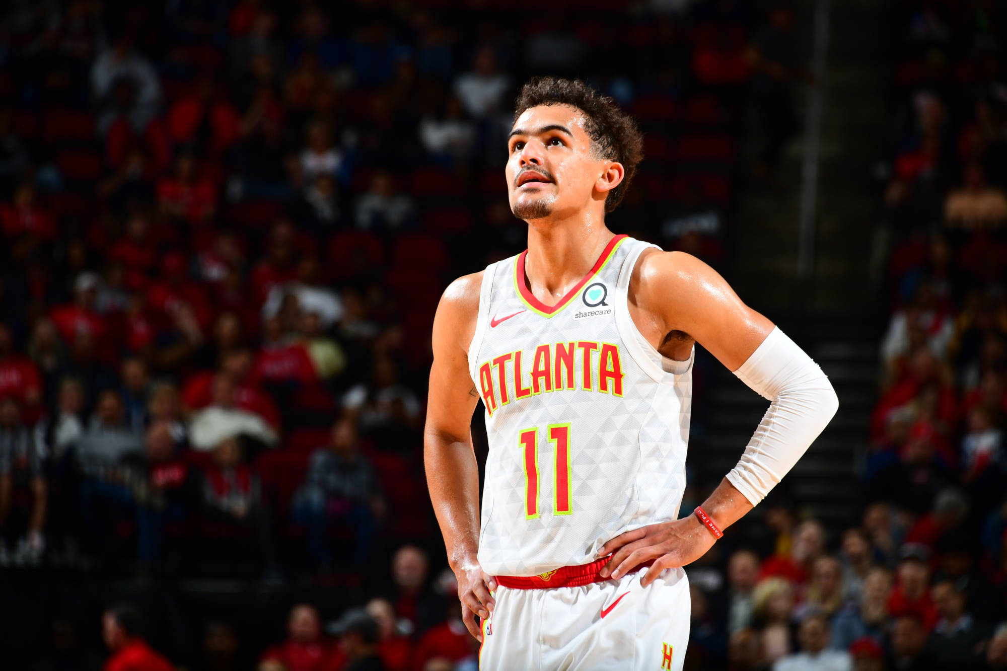 Trae Young 桌布 壁紙 — 一位專注的亞特蘭大老鷹隊籃球運動員，身穿白色11號球衣，在場館燈光下手叉腰站立。