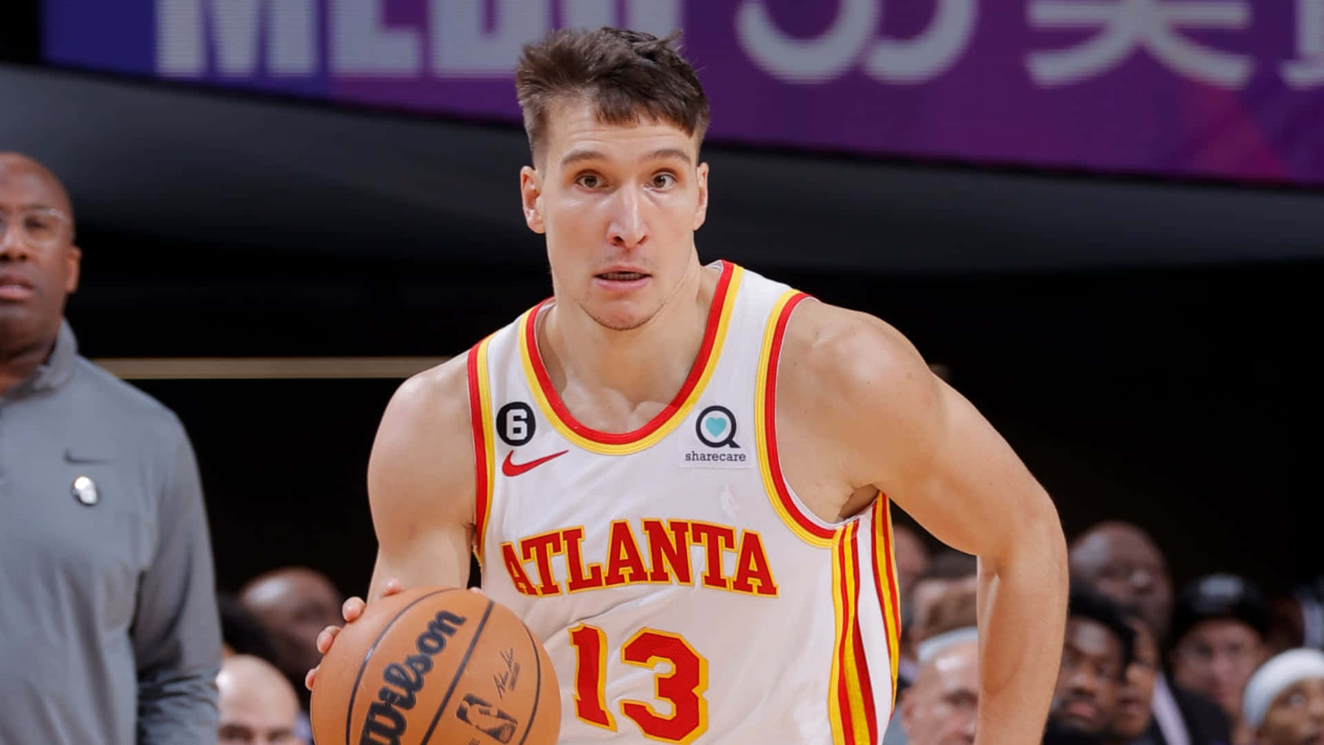 NBA 桌布 壁紙 — 一位專注的亞特蘭大老鷹隊籃球運動員，身穿白色和紅色球衣，在明亮的場館燈光下於比賽中運著威爾遜籃球。