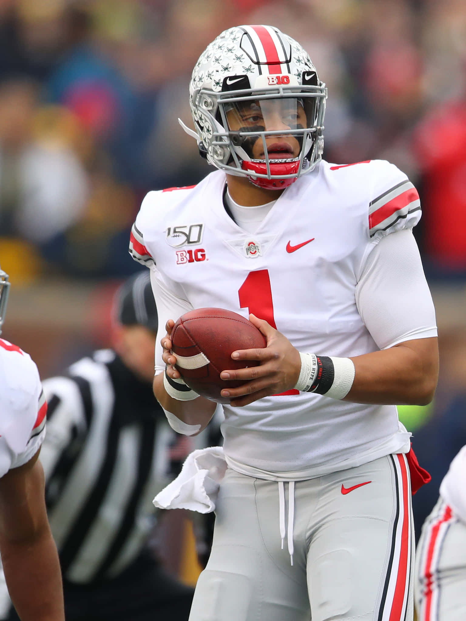 Justin Fields 桌布 壁紙 — 一位專注的俄亥俄州立大學美式足球四分衛身穿白色球衣、背號1號，在陽光明媚的球場上持球進行比賽。