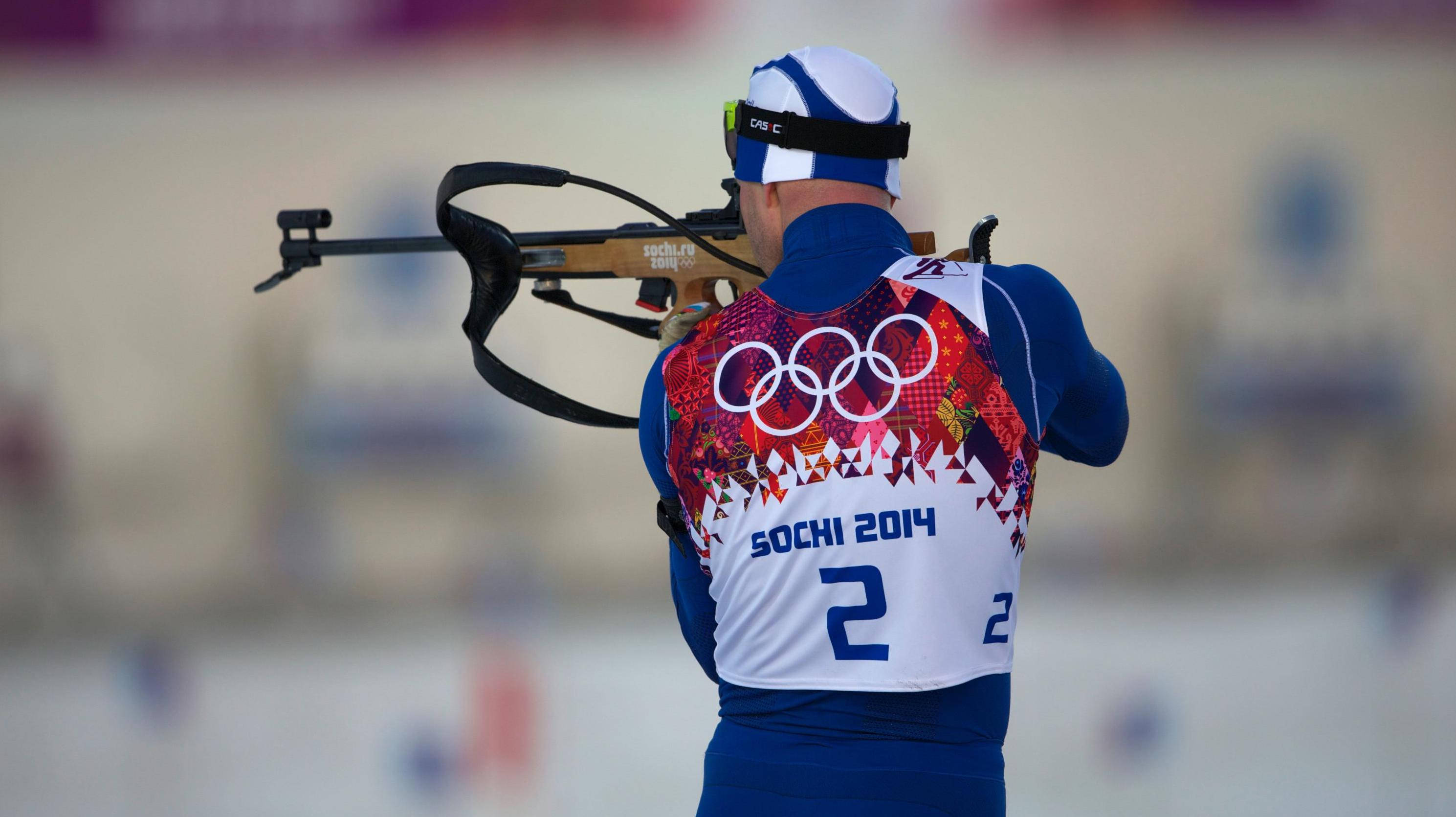 運動 桌布 壁紙 — 一位專注的冬季冬季兩項運動員身穿藍色索契2014裝備，在比賽中瞄準十字弓，背上可見奧運五環。