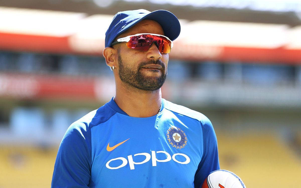 shikhar dhawan 桌布 壁紙 — 一位專注的印度板球運動員穿著藍色訓練裝備，在體育場明亮的日光下拿著一個球。