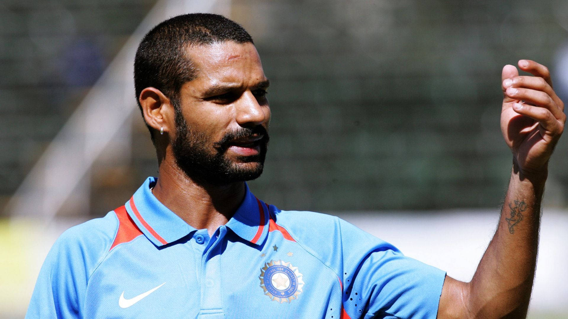 shikhar dhawan 桌布 壁紙 — 一位專注的印度板球運動員穿著藍色球衣，在陽光明媚的戶外練習中做手勢。