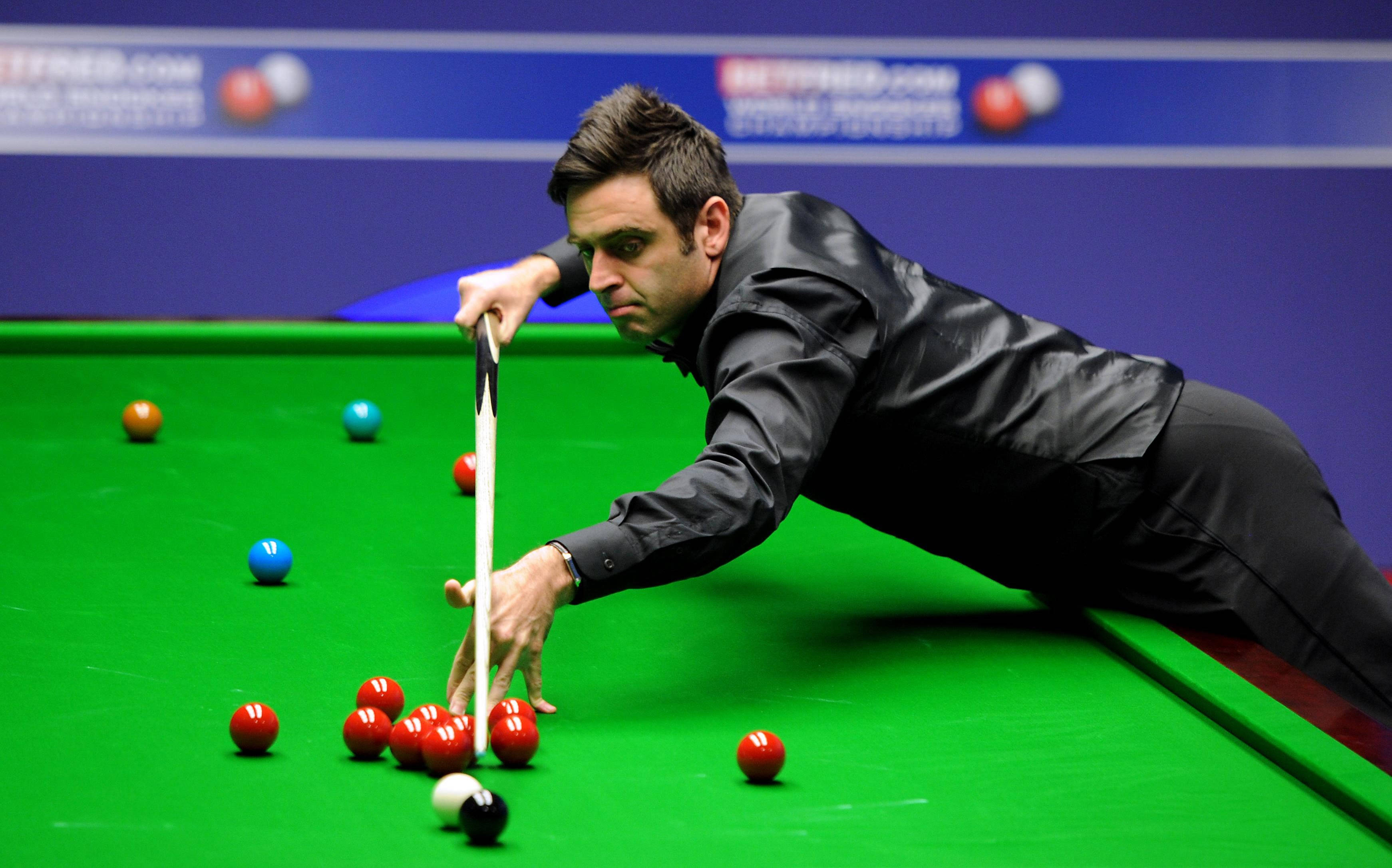 Snooker 桌布 壁紙 — 一位專注的司諾克球員身穿黑色西裝，俯身於綠色球檯上，用球桿瞄準一組紅球。