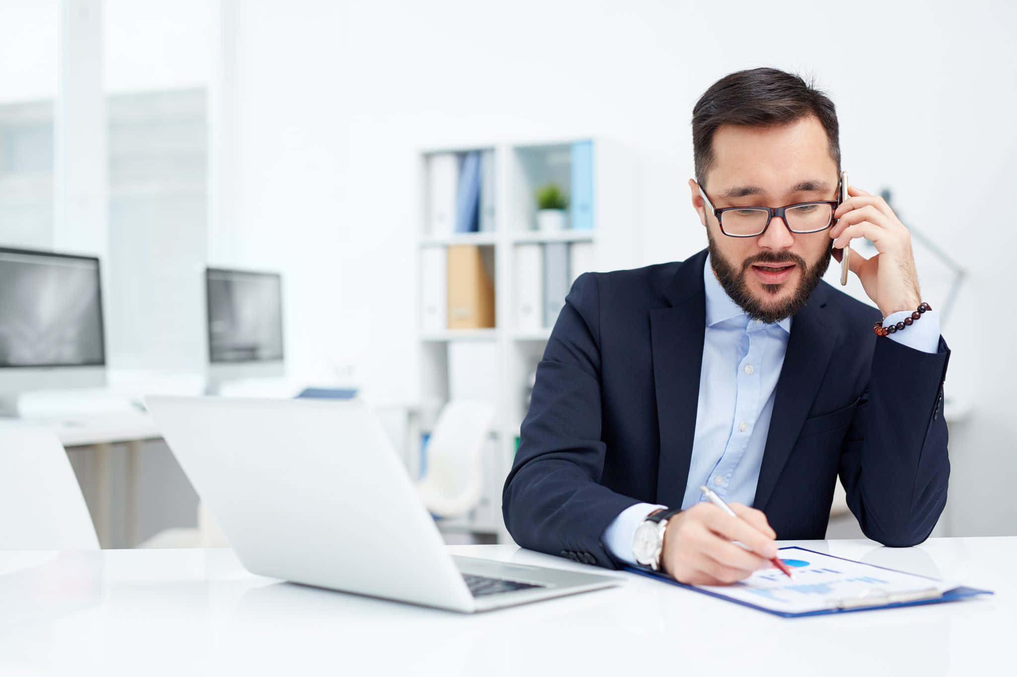 Telemarketing 桌布 壁紙 — 一位專注的商務人士穿著西裝，在明亮現代辦公桌上簽署文件時正在通電話。