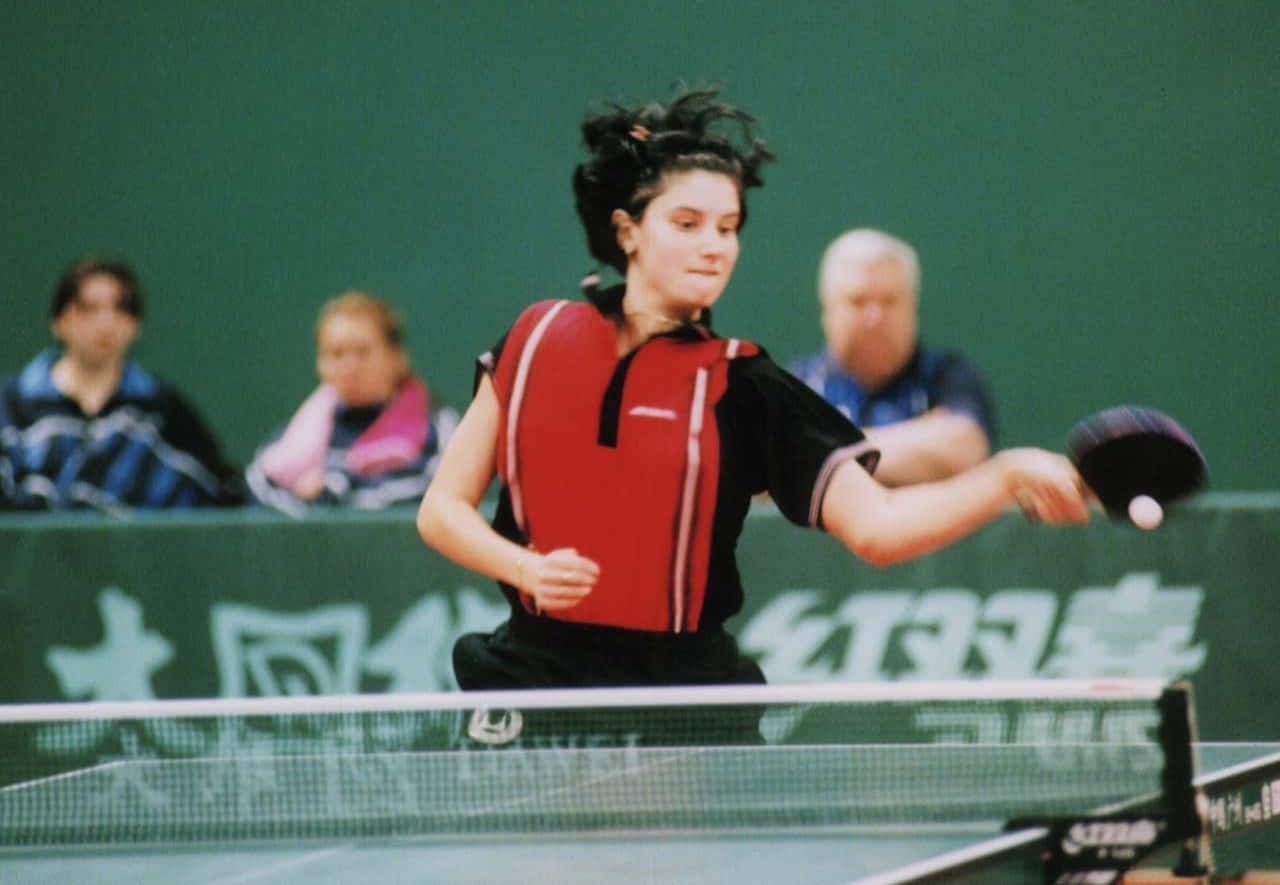 Table Tennis 桌布 壁紙 — 一位專注的女乒乓球選手，身穿紅黑裝備，在激烈的比賽中揮拍擊球。