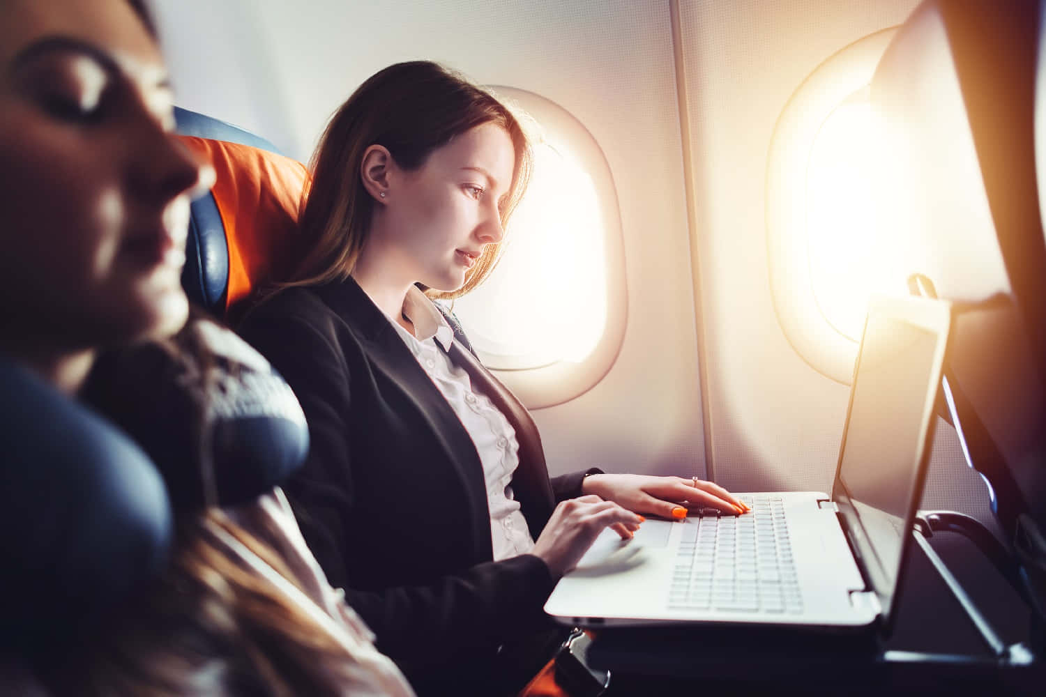 Travel Desktop 桌布 壁紙 — 一位專注的女商人在飛機窗邊打字，金色陽光灑入照亮她的工作空間。