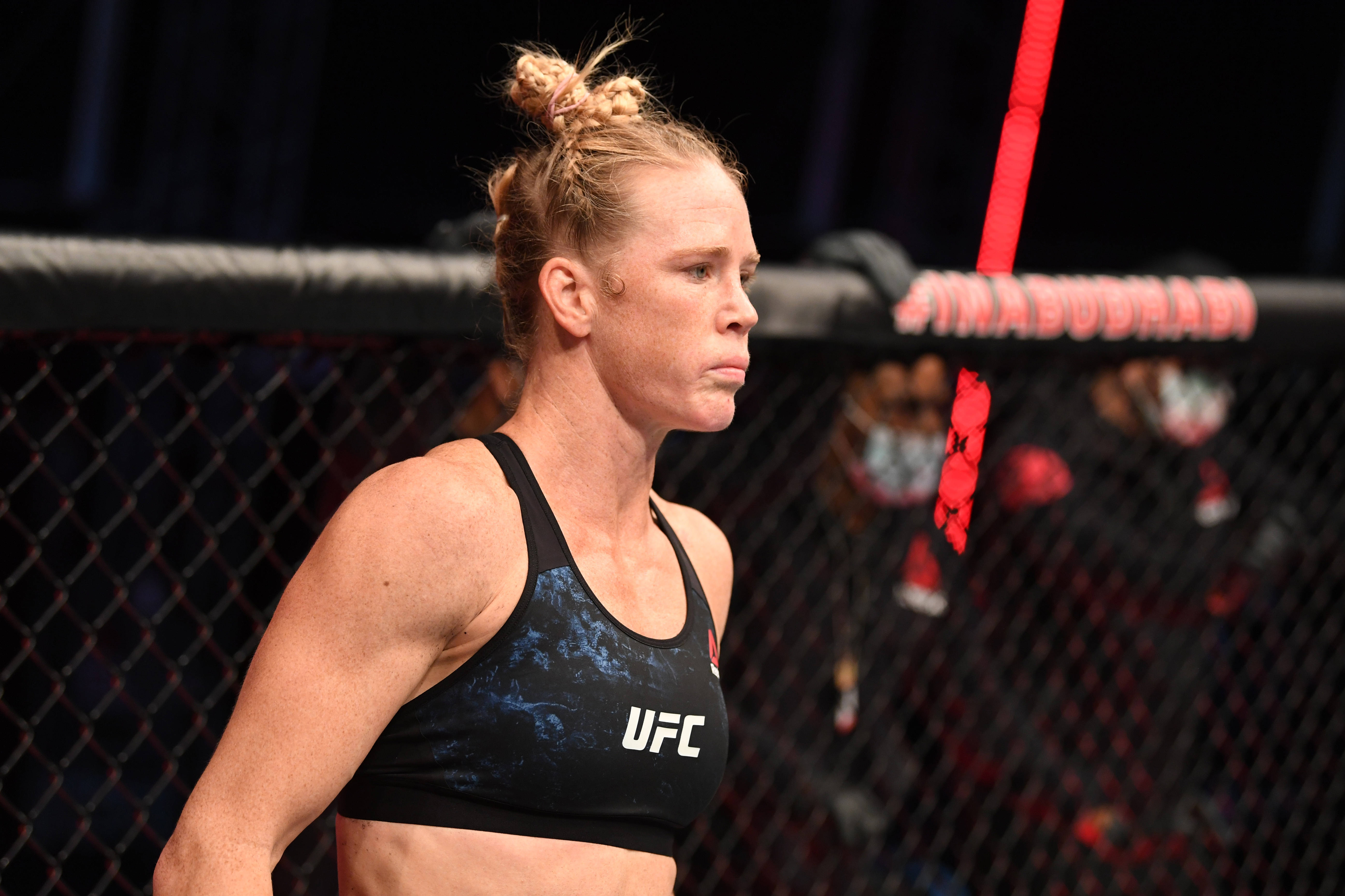 Fight 桌布 壁紙 — 一位專注的女性MMA拳手穿著UFC運動胸罩，站在八角籠內，表情堅定。