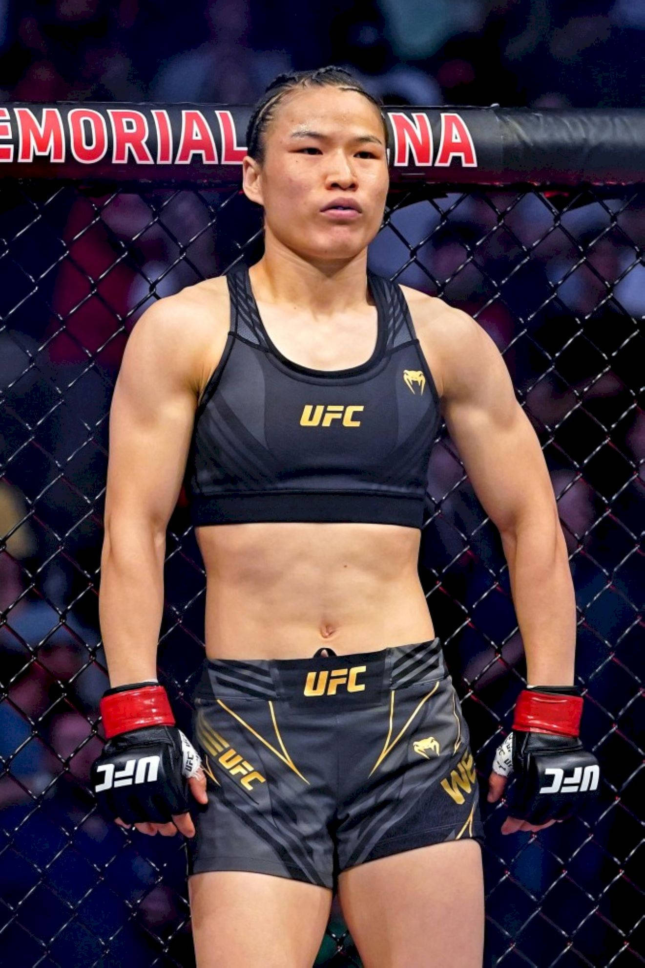 Athletic 桌布 壁紙 — 一位專注的女性MMA拳手穿著UFC裝備，站在明亮的場館燈光下的八角籠內。