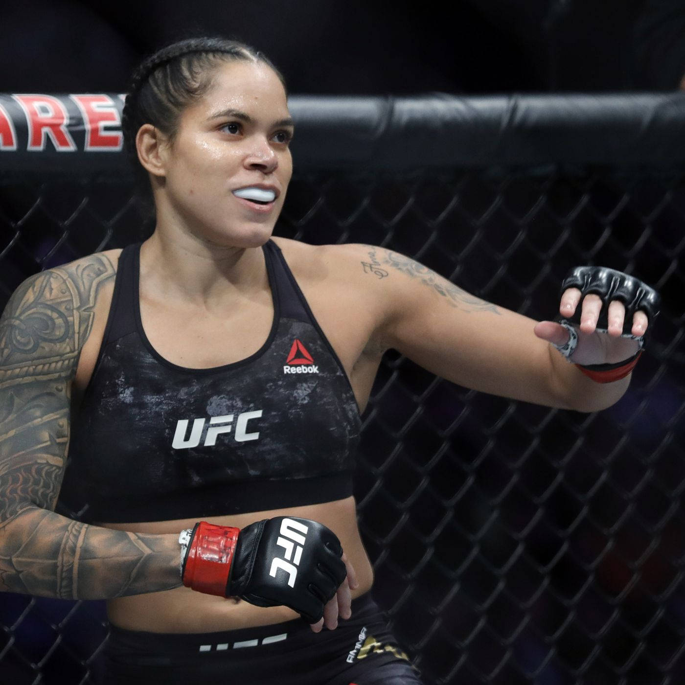 UFC 桌布 壁紙 — 一位專注的女性MMA拳手身穿UFC裝備，站在八角籠內，手臂上的刺青清晰可見。