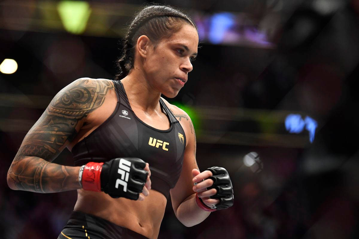 UFC 桌布 壁紙 — 一位專注的女性UFC拳手，手臂上有刺青，在八角籠內、場館燈光下準備就緒。