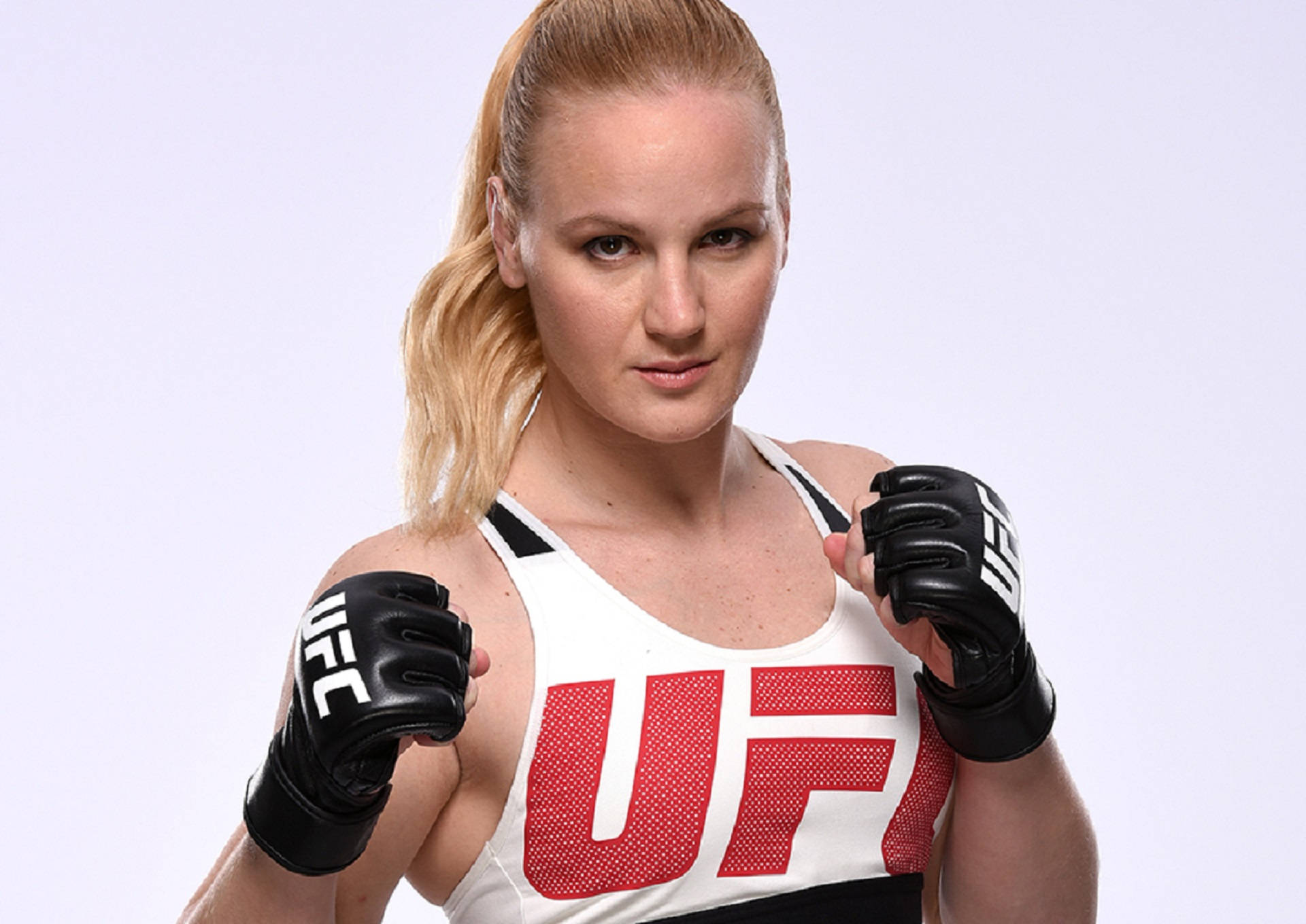 valentina 桌布 壁紙 — 一位專注的女性UFC拳手，身穿白色和紅色裝備，戴著黑色手套，在純白色背景前擺姿勢。