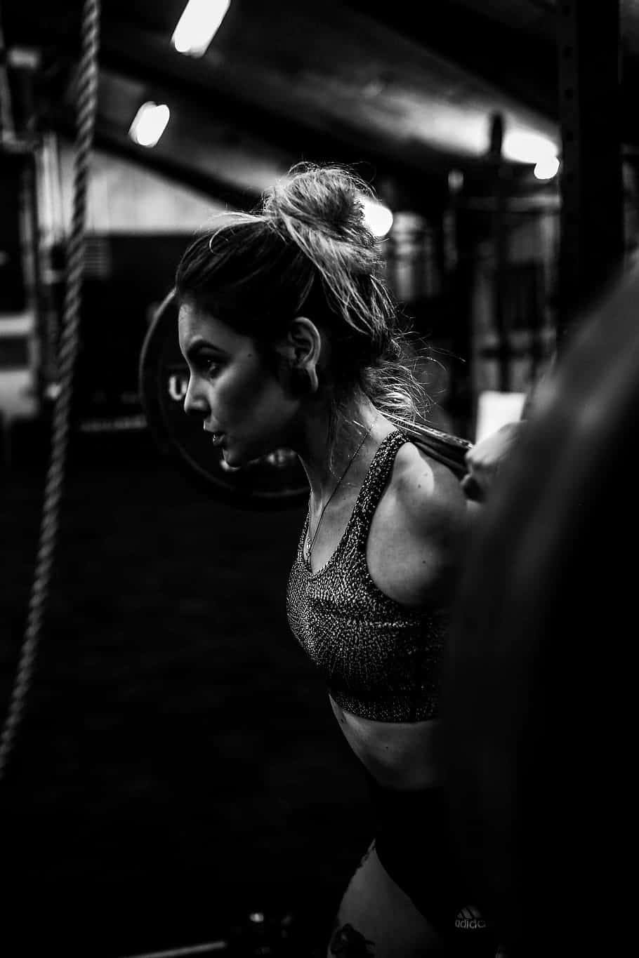 Fitness 桌布 壁紙 — 一位專注的女性在健身房舉起槓鈴，以強烈燈光拍攝出戲劇性的黑白照片。