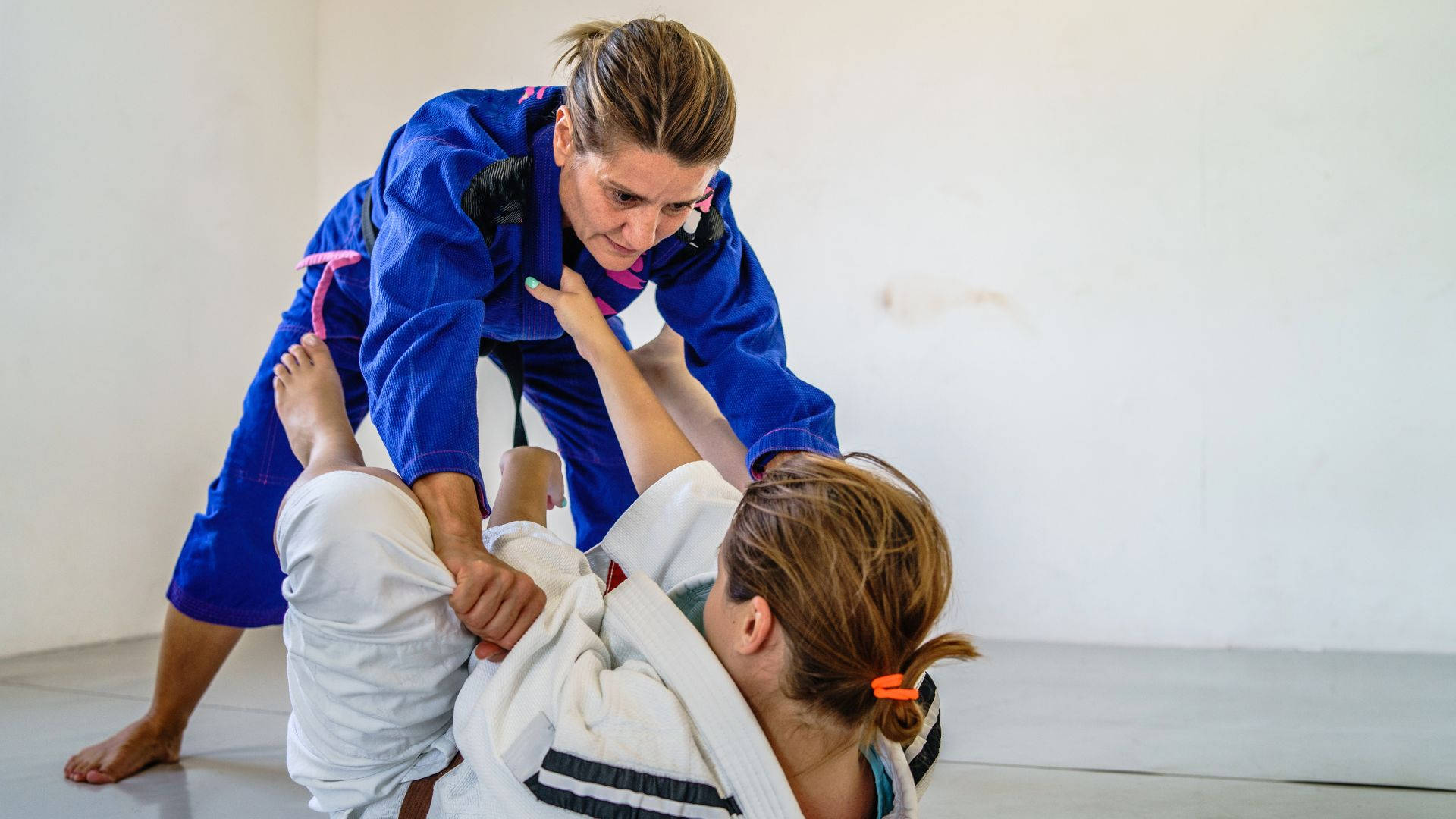 martial arts 桌布 壁紙 — 一位專注的女性穿著藍色柔道服，在訓練期間對另一位穿著白色道服的女性施展纏鬥技術。