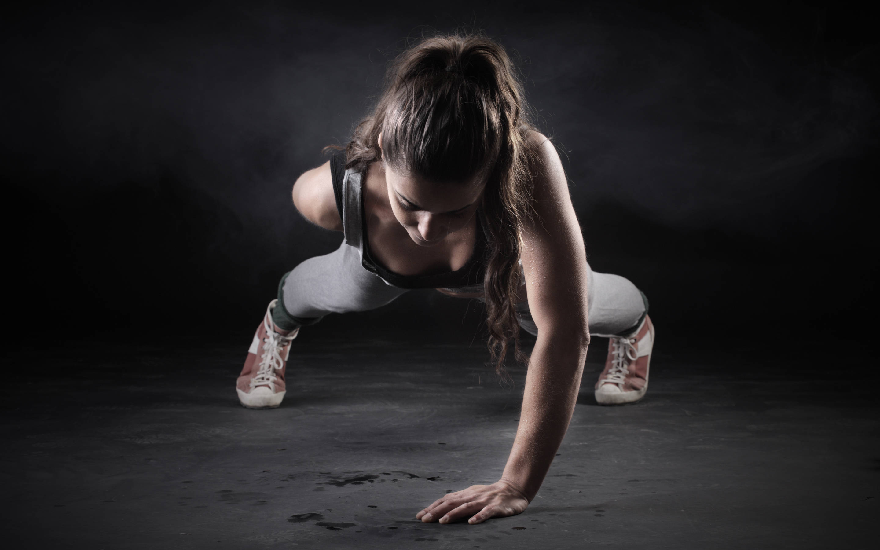 Exercise 桌布 壁紙 — 一位專注的女性穿著運動裝備，在戲劇性工作室燈光下的黑暗煙霧地板上做伏地挺身。