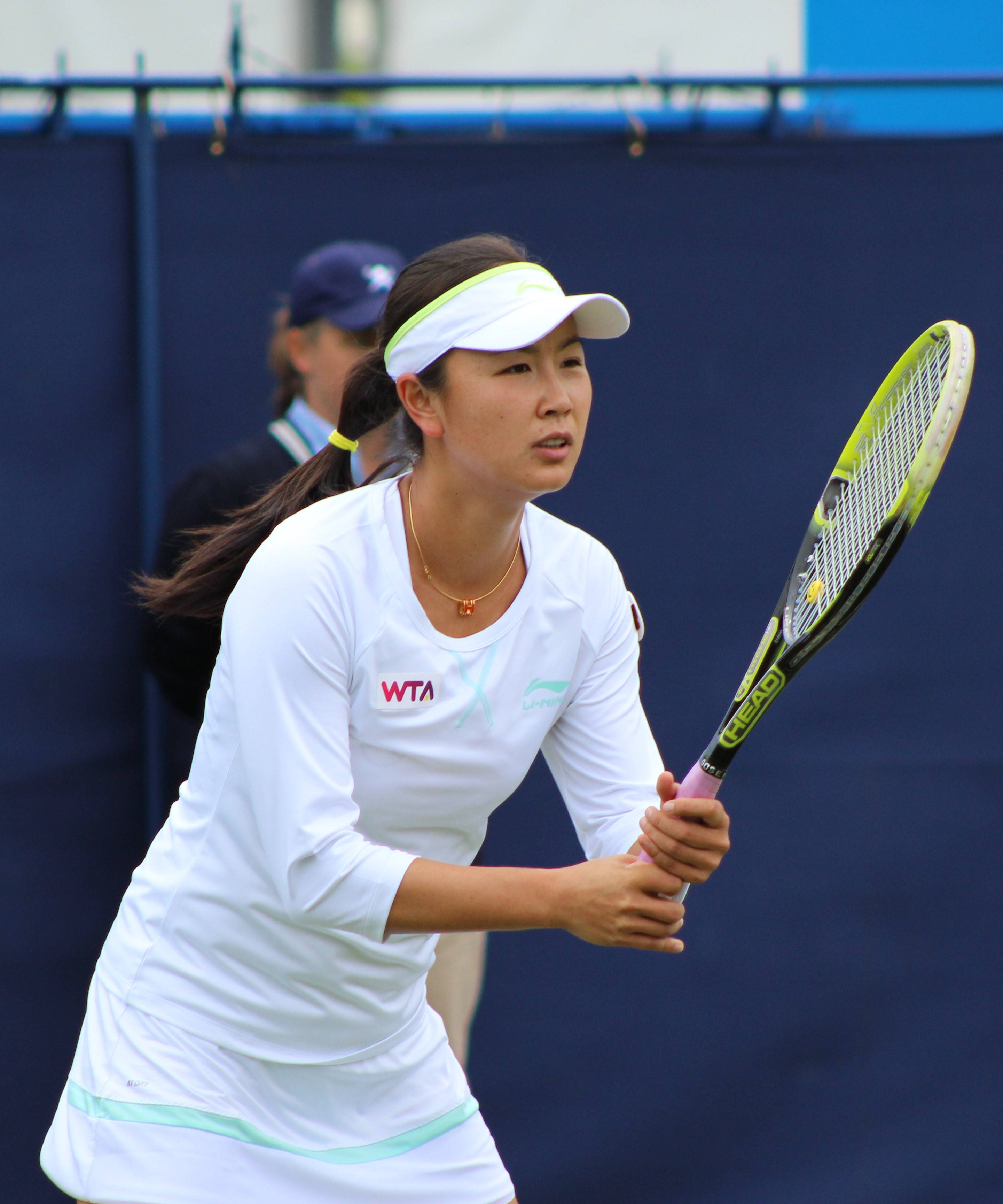 Tennis 桌布 壁紙 — 一位專注的女性網球運動員身穿白色裝備，在藍色球場上揮拍中緊握著萊姆綠色的球拍。