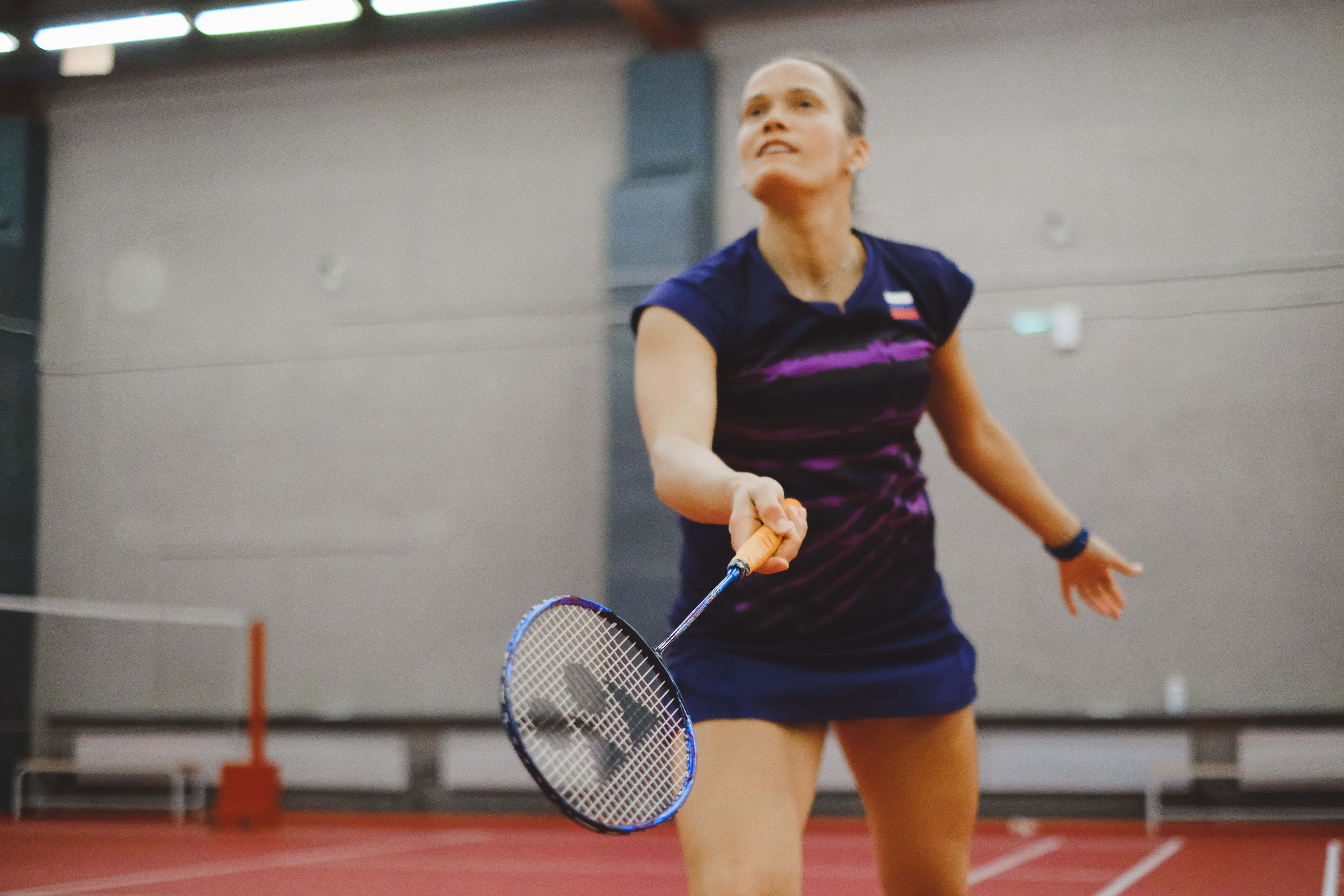 Badminton 桌布 壁紙 — 一位專注的女性羽毛球運動員在室內場地移動，球拍在揮拍中途伸展。