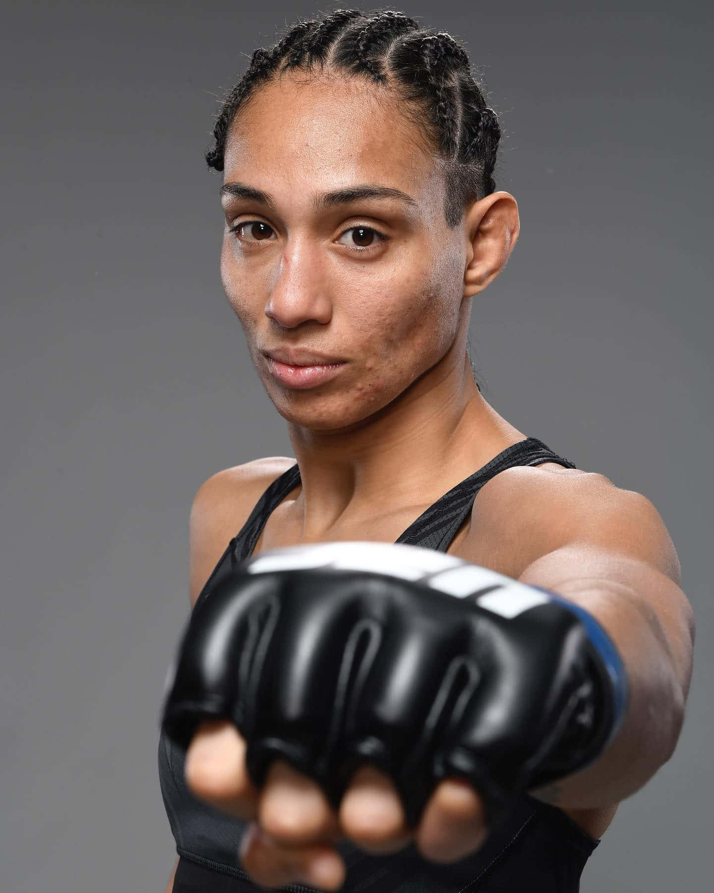 UFC 桌布 壁紙 — 一位專注的女戰士戴著黑色手套，在灰色中性背景前，凝視著鏡頭並伸出拳頭。