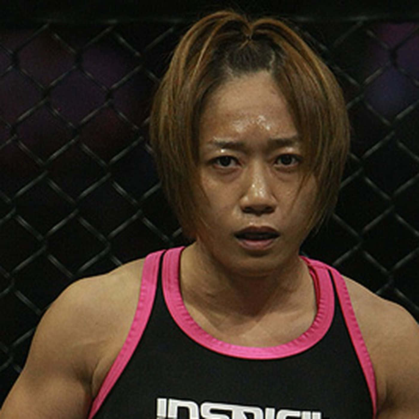UFC 桌布 壁紙 — 一位專注的女戰士穿著黑色粉紅邊背心，在昏暗的MMA八角籠內凝視著。