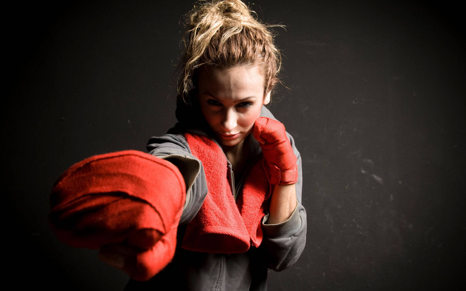 Boxing 桌布 壁紙 — 一位專注的女拳擊手戴著紅色手套，在黑暗的攝影棚背景下以戲劇性的燈光向前出擊。