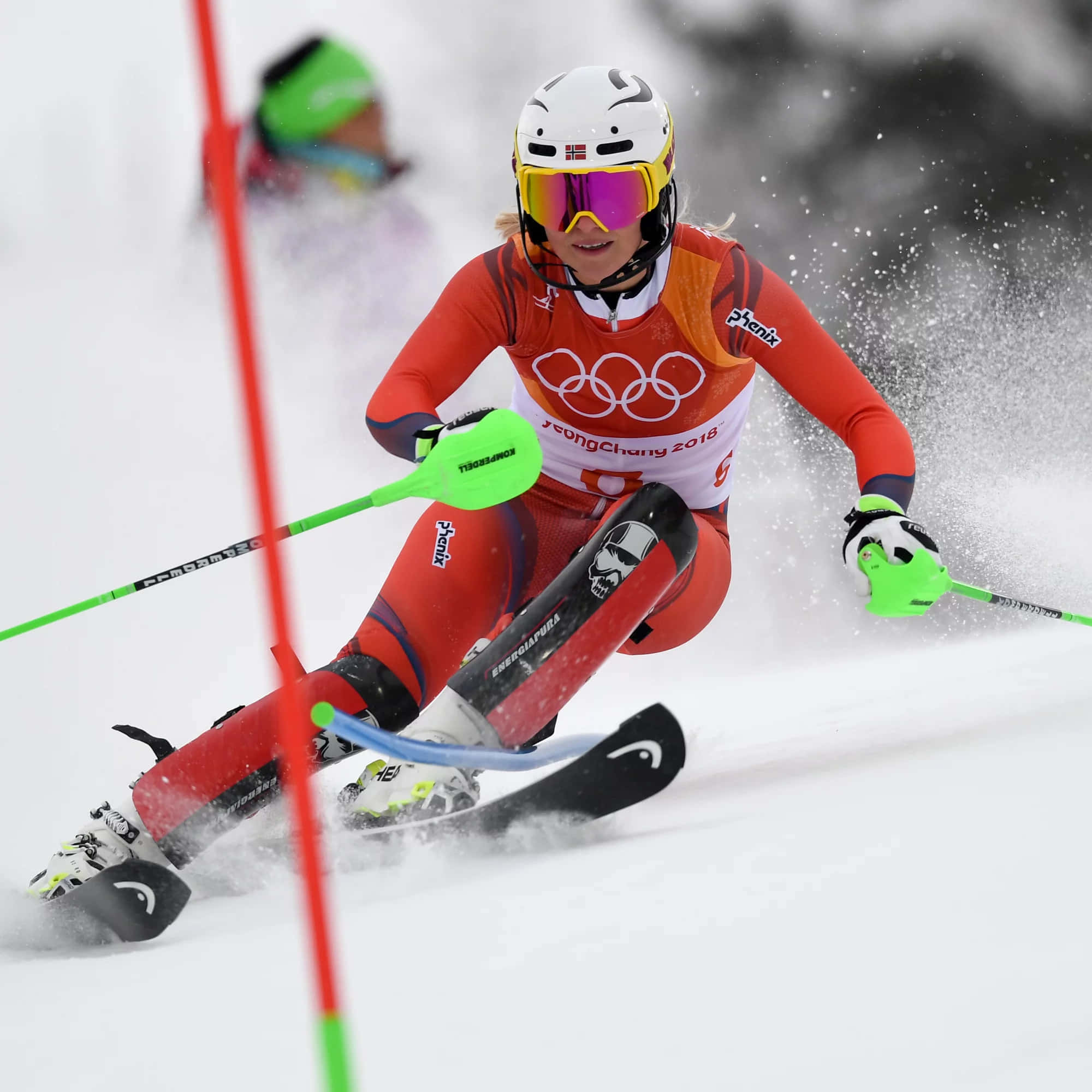 ski 桌布 壁紙 — 一位專注的女滑雪運動員穿著紅色奧運裝備，在競爭性下坡比賽中繞過紅色閘門在雪中滑行。