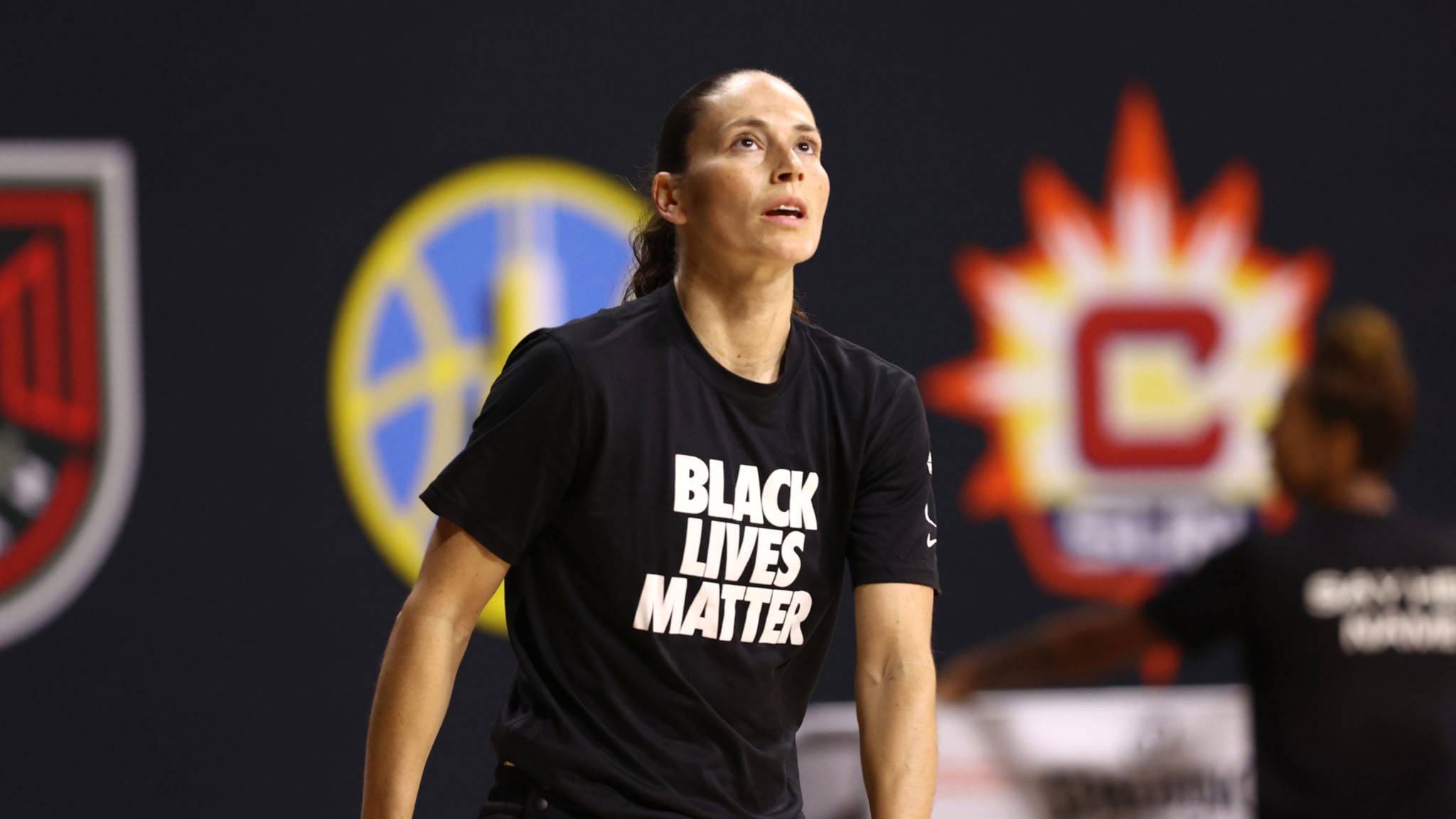 Sue 桌布 壁紙 — 一位專注的女籃球員穿著黑色「BLACK LIVES MATTER」T恤，站在球場上，身後有球隊標誌。