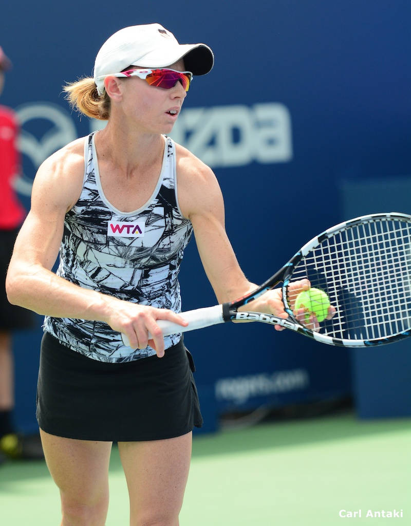 Tennis 桌布 壁紙 — 一位專注的女網球運動員，戴著白色帽子，穿著黑色裙子，在綠色球場上準備用 Babolat 球拍發球。
