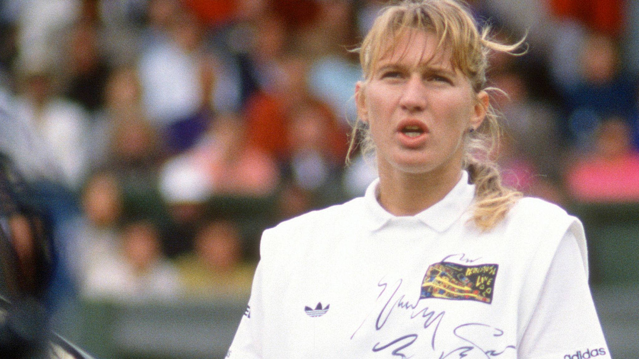 Tennis 桌布 壁紙 — 一位專注的女網球運動員，身穿帶有簽名和標誌的白色adidas球衣，比賽中背景有觀眾。