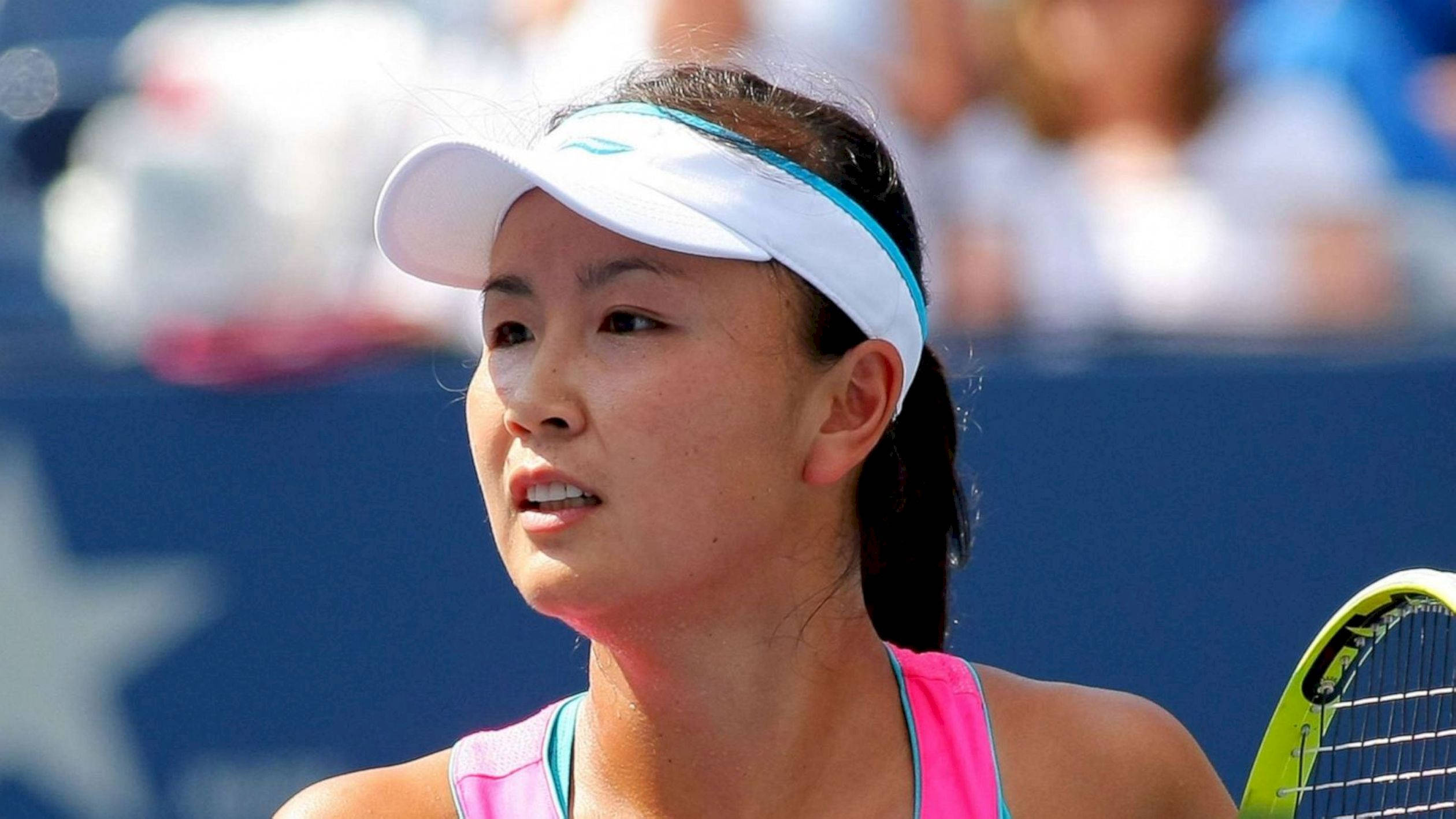 運動 桌布 壁紙 — 一位專注的女網球運動員，身穿粉紅色上衣和白色遮陽帽，在明亮的日光下比賽中緊握球拍。