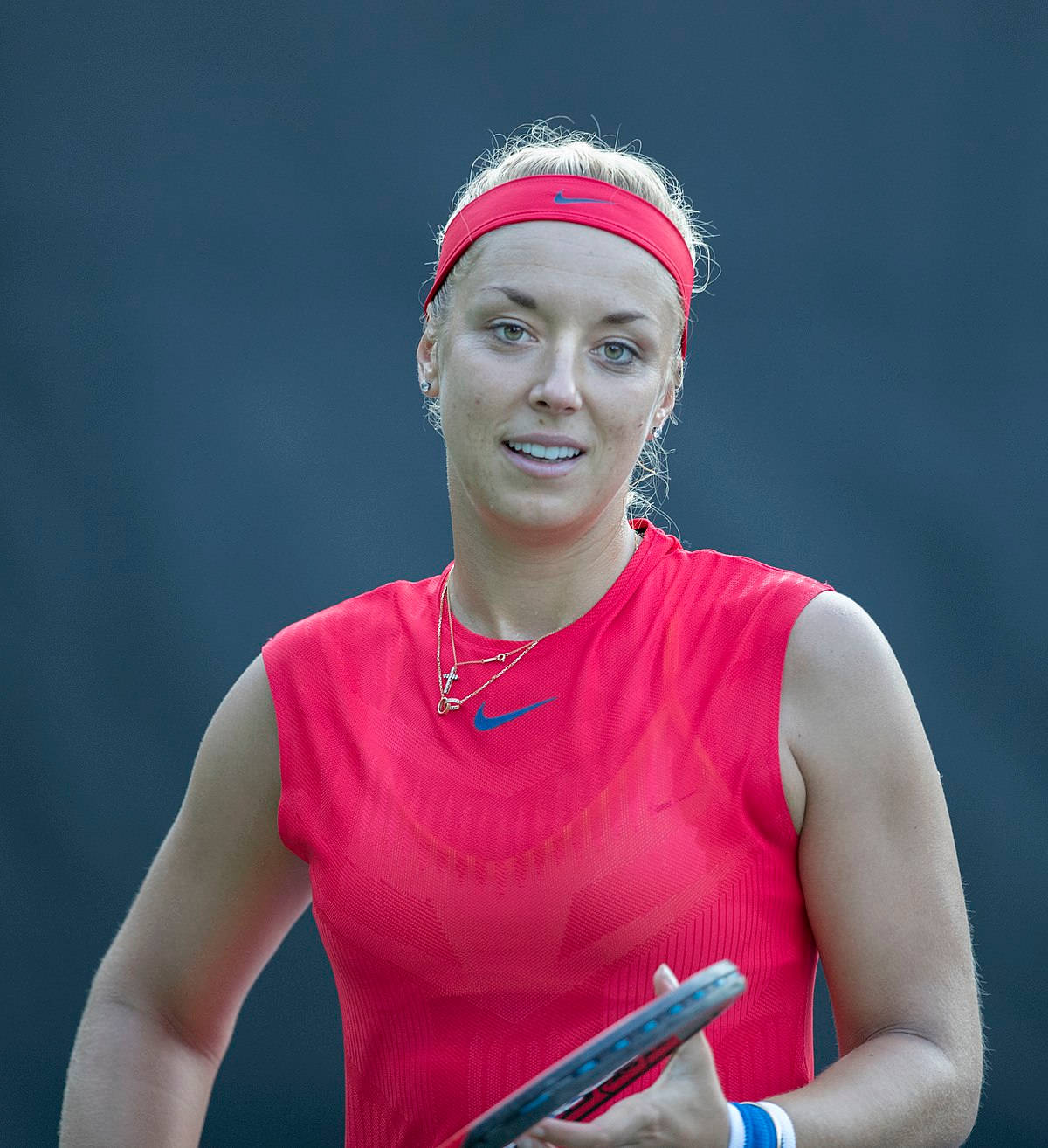 Tennis 桌布 壁紙 — 一位專注的女網球運動員，身穿鮮紅色無袖上衣和相配的頭帶，在深藍色背景下握著球拍。