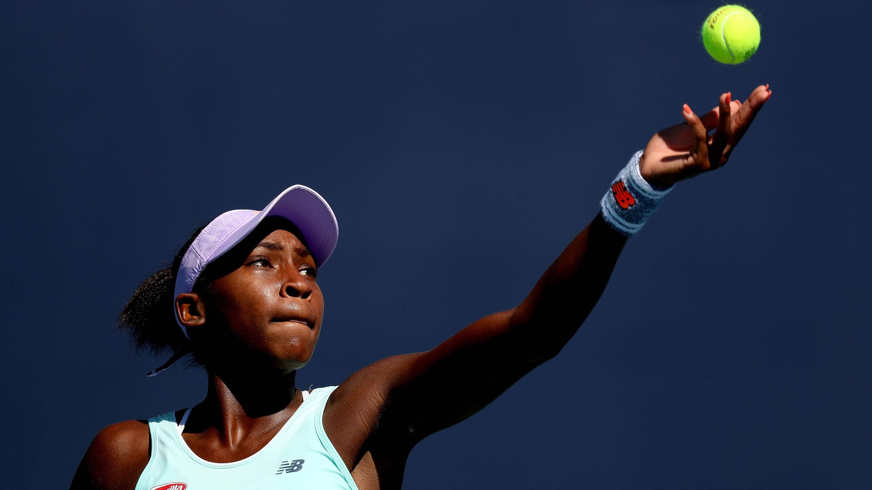 Coco Gauff 桌布 壁紙 — 一位專注的女網球運動員將一顆亮黃色的球拋向深藍色的天空。