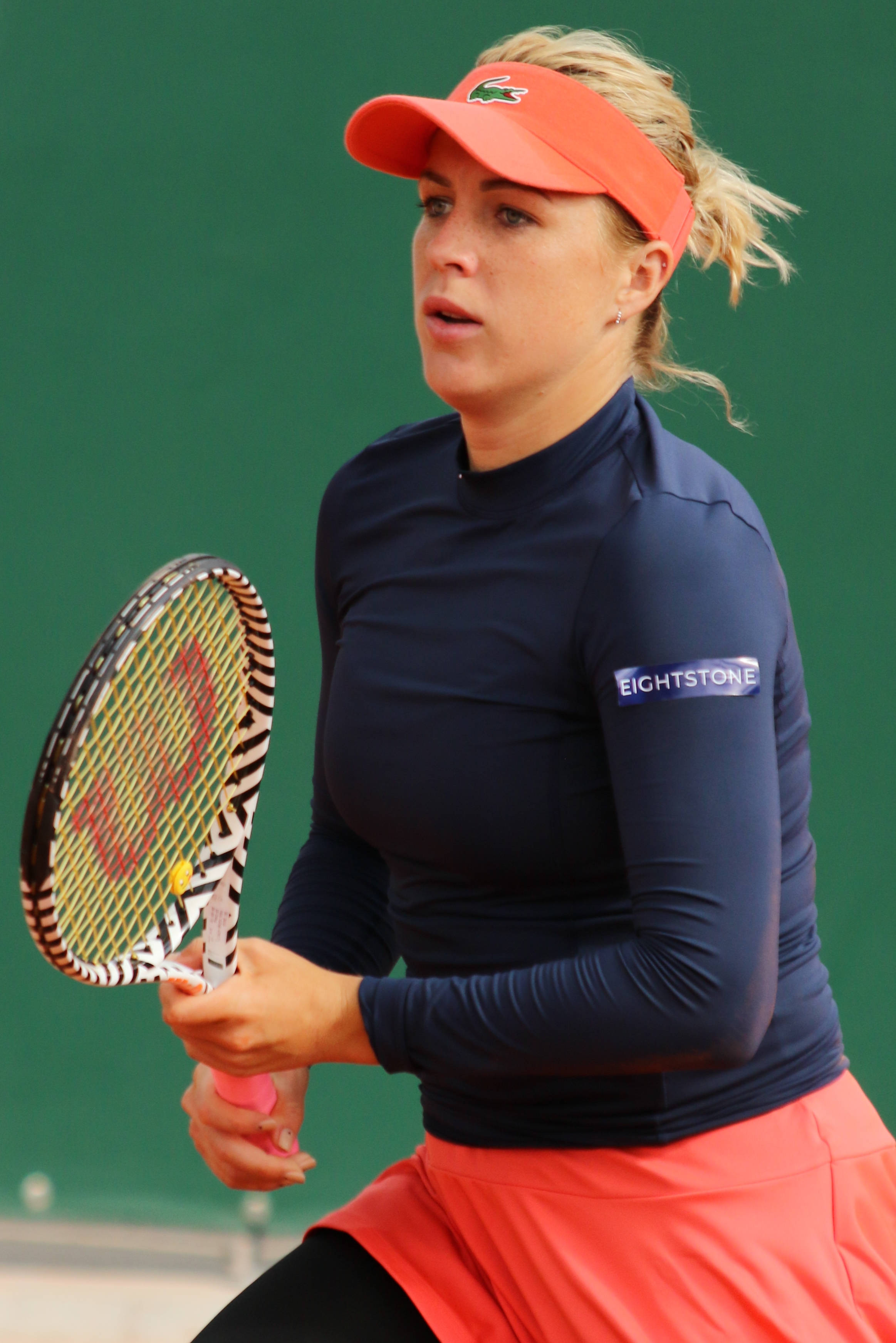Tennis 桌布 壁紙 — 一位專注的女網球運動員穿著海軍藍和珊瑚色裝備，在綠色球場背景下揮拍中握緊球拍。