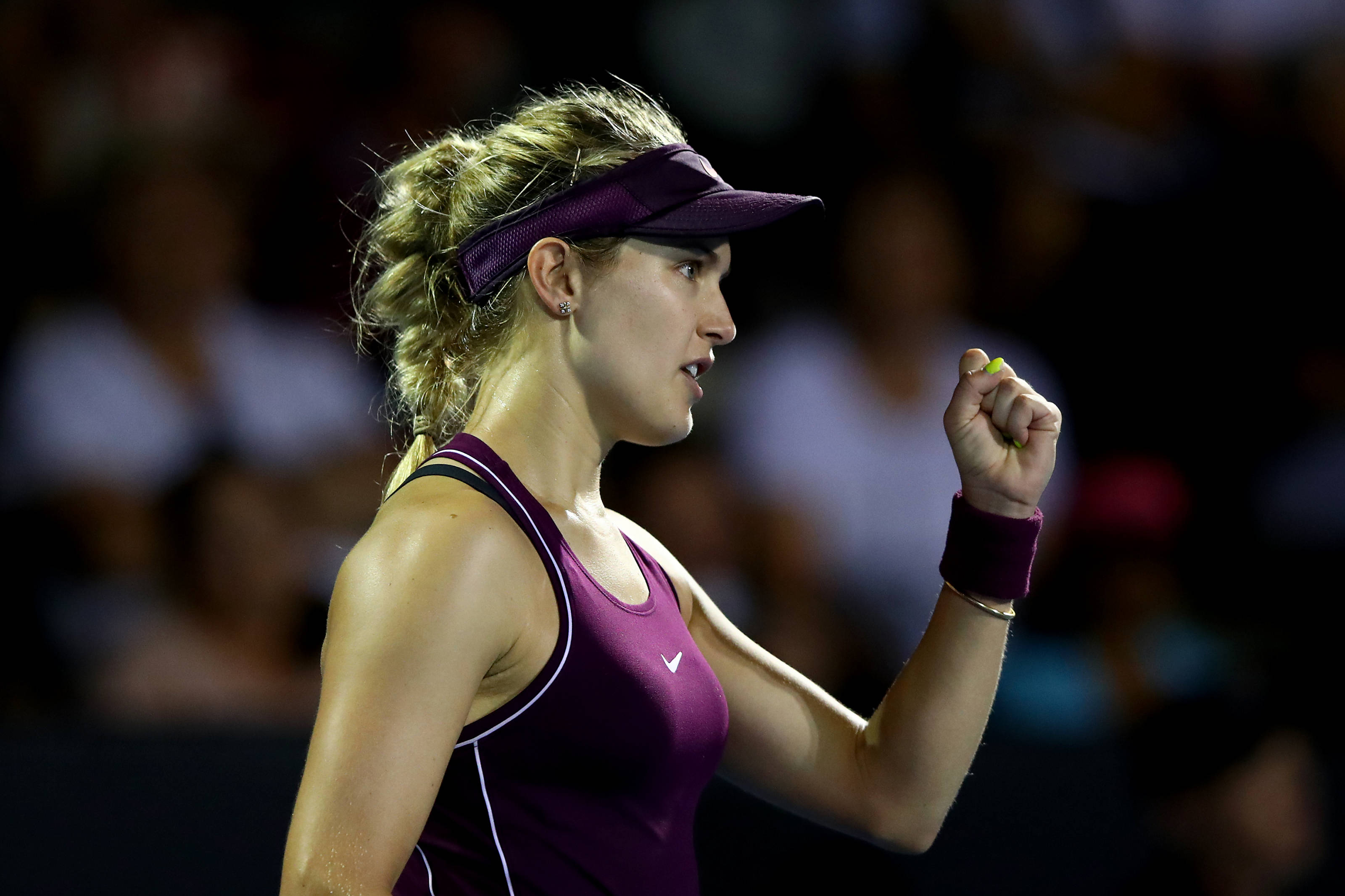 Tennis 桌布 壁紙 — 一位專注的女網球運動員穿著紫色服裝，在明亮的體育場燈光下比賽中握緊拳頭。
