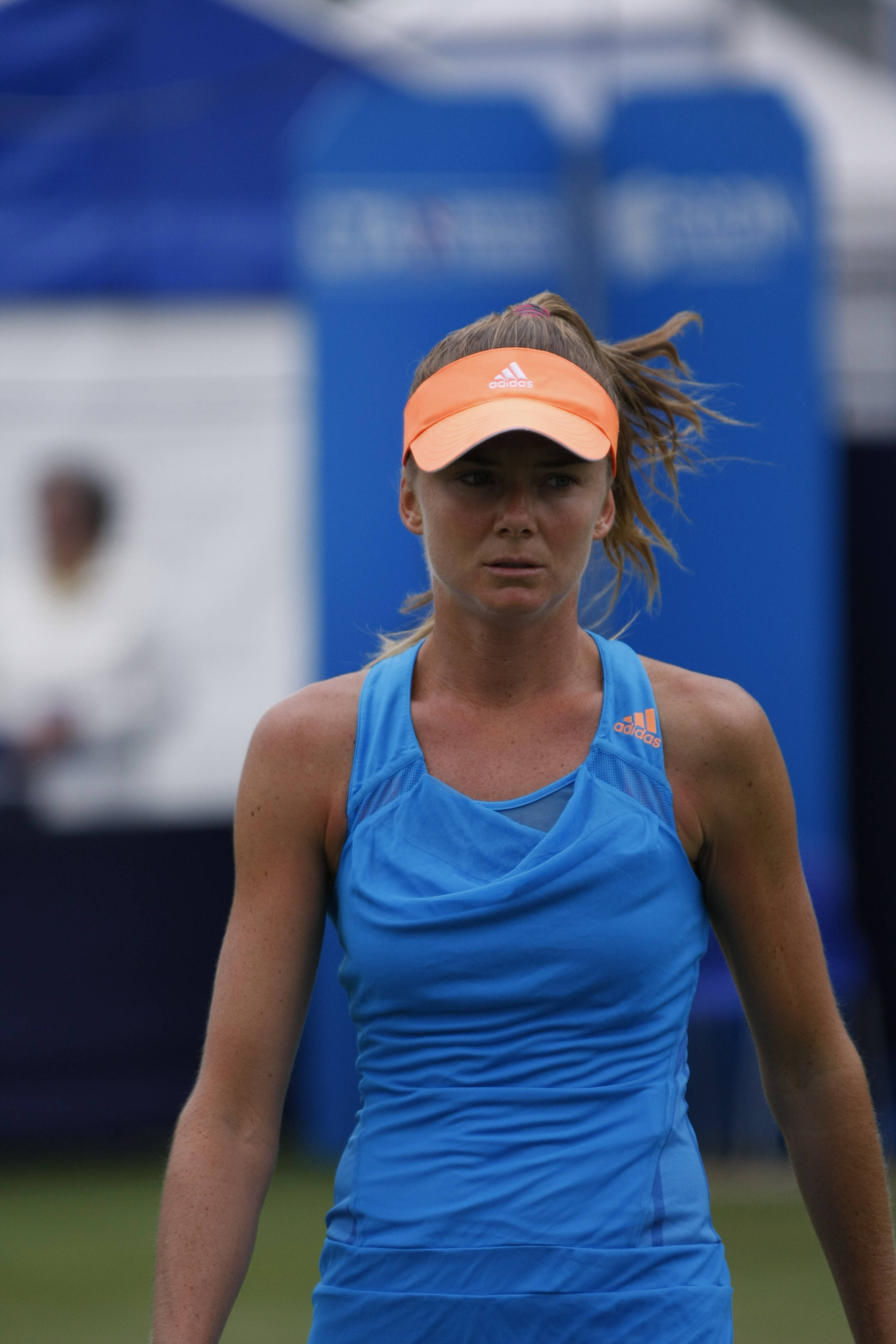Tennis 桌布 壁紙 — 一位專注的女網球運動員穿著藍色運動服和橙色遮陽帽，站在草地上，風吹動她的頭髮。