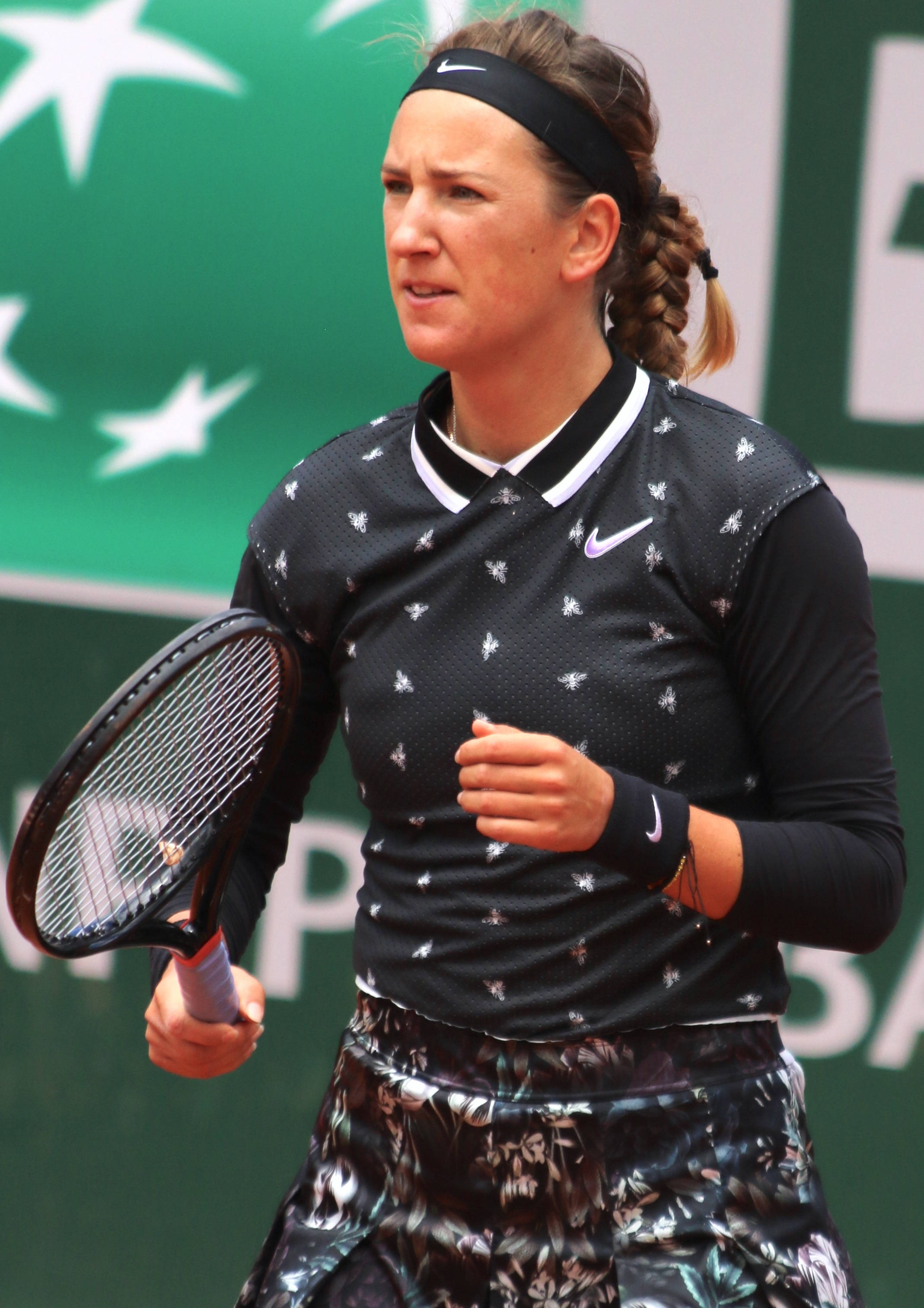 Athletic 桌布 壁紙 — 一位專注的女網球運動員穿著黑色運動裝備，在背景有白色星星的綠色球場上比賽中握著球拍。