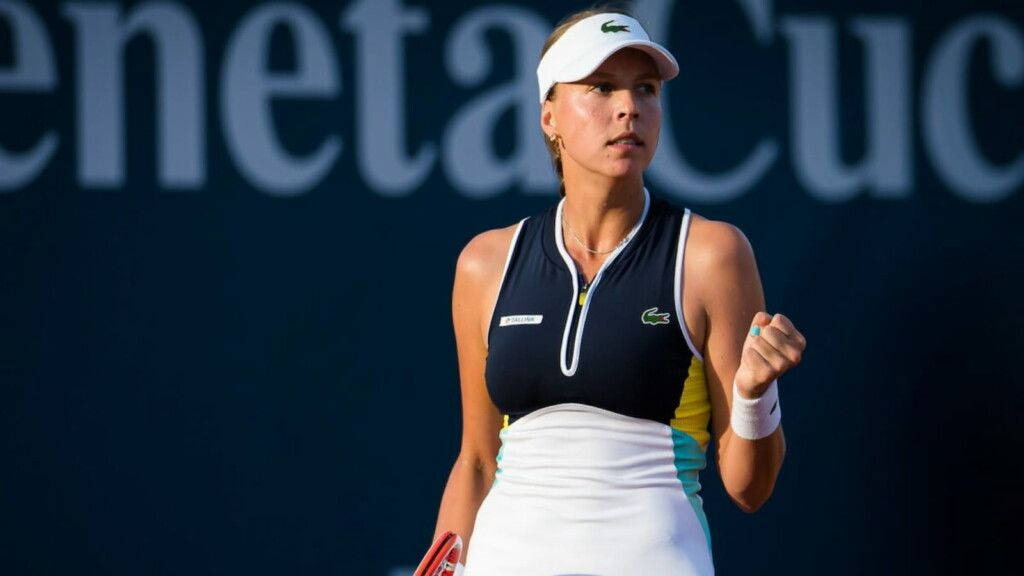 Athletic 桌布 壁紙 — 一位專注的女網球運動員身穿海軍藍和白色服裝，在球場上比賽中握緊拳頭，背景是模糊的「Simona Halep」。