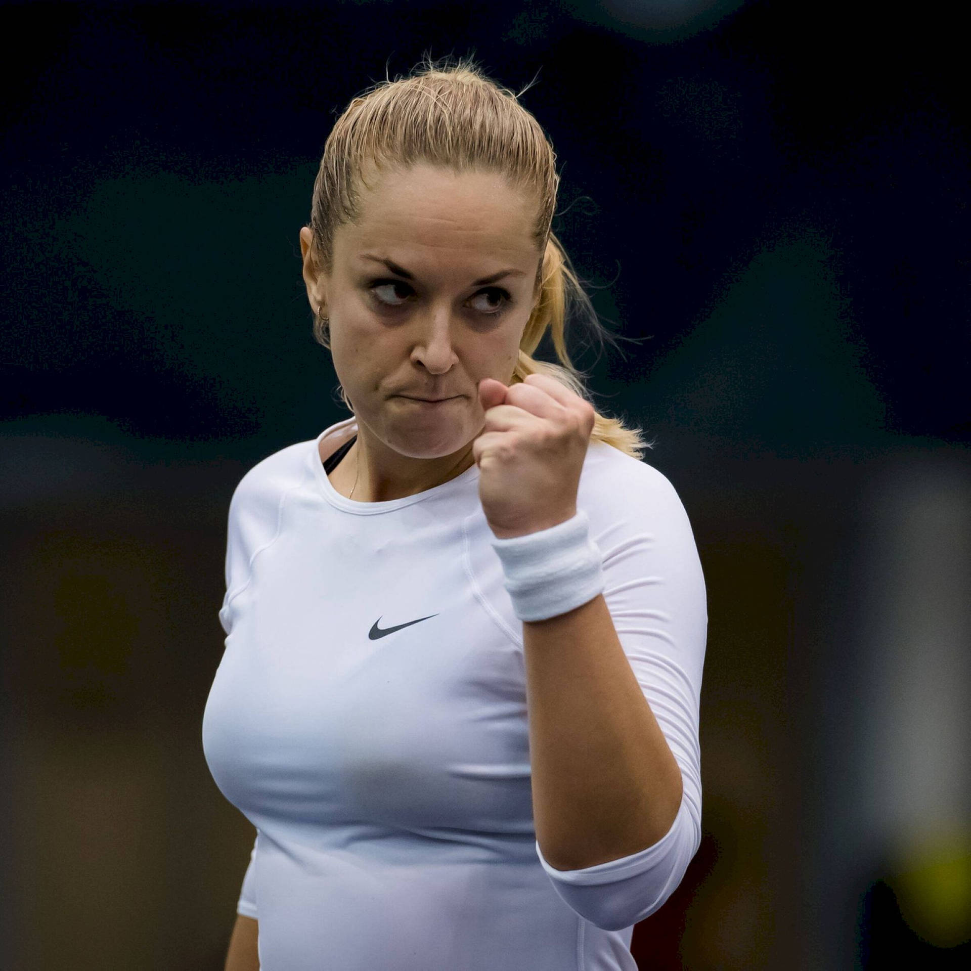 Tennis 桌布 壁紙 — 一位專注的女網球運動員身穿白色Nike衫，在模糊的深色背景下握緊拳頭，充滿決心。