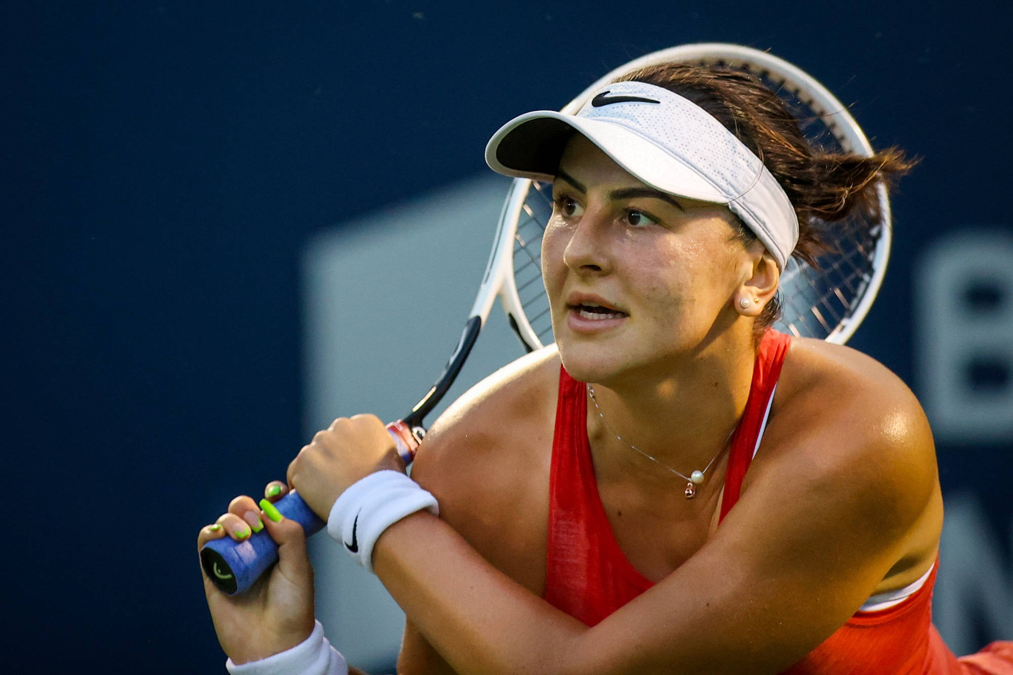 Bianca Andreescu 桌布 壁紙 — 一位專注的女網球運動員身穿紅色運動服和白色遮陽帽，在深藍色球場背景下揮拍中緊握球拍。