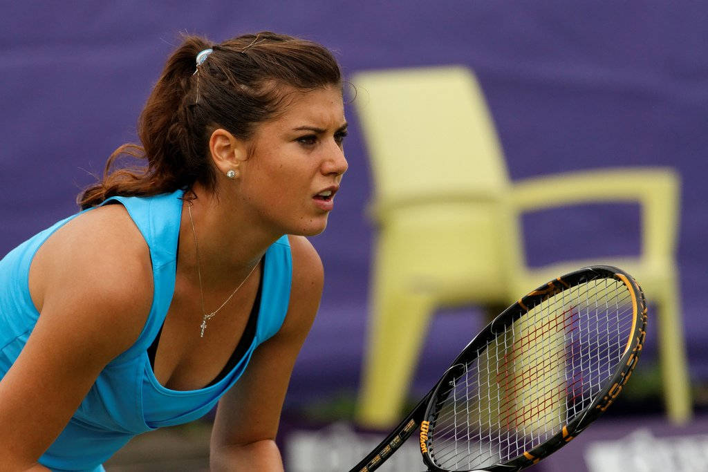 Tennis 桌布 壁紙 — 一位專注的女網球運動員身穿藍色上衣，在紫色背景的球場上蹲下，準備好球拍。
