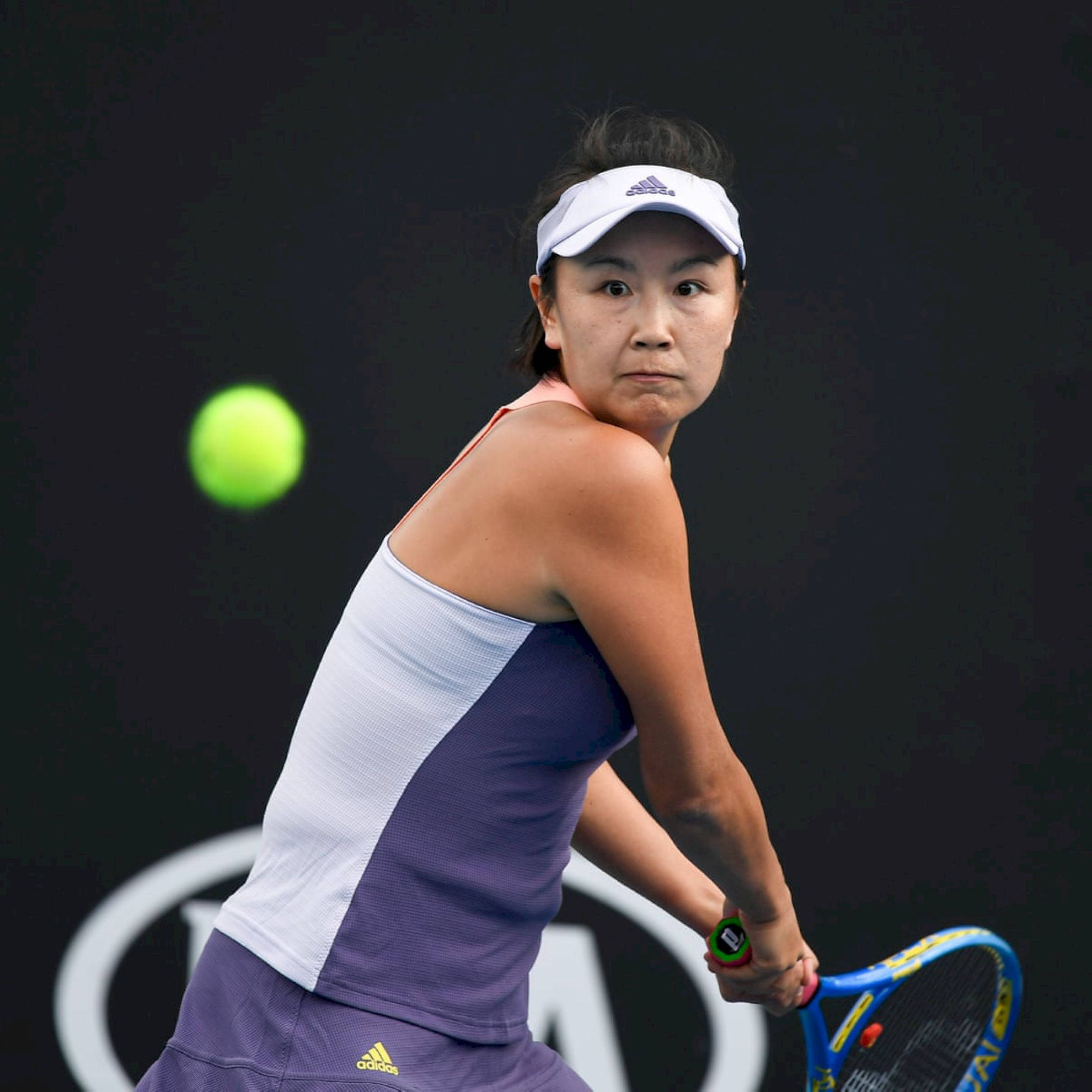 Tennis 桌布 壁紙 — 一位專注的女網球選手，身穿紫色和白色裝備，在深色背景下揮拍擊打一個亮綠色的球。