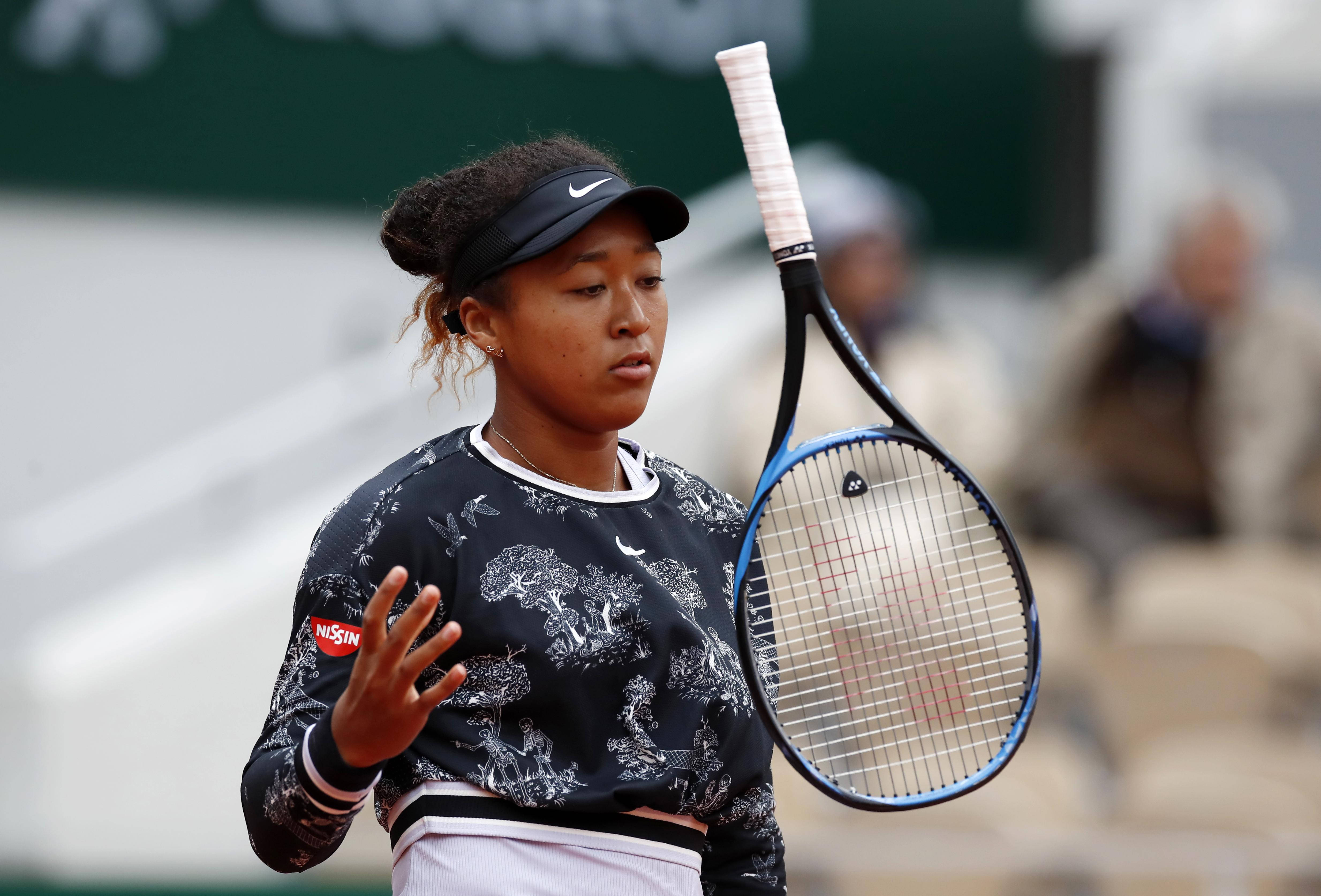 naomi 桌布 壁紙 — 一位專注的女網球選手在紅土球場比賽中握著球拍，背景有模糊的觀眾。