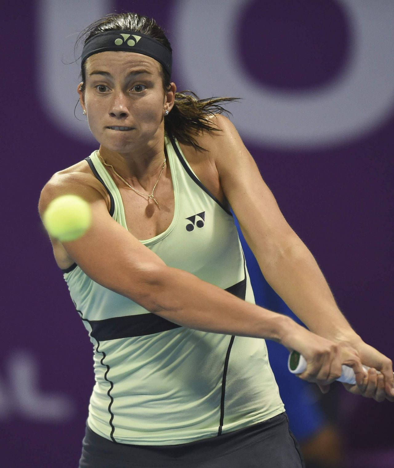 Tennis 桌布 壁紙 — 一位專注的女網球選手在紫色體育場燈光下進行激烈比賽時揮拍擊打明亮的黃色球。