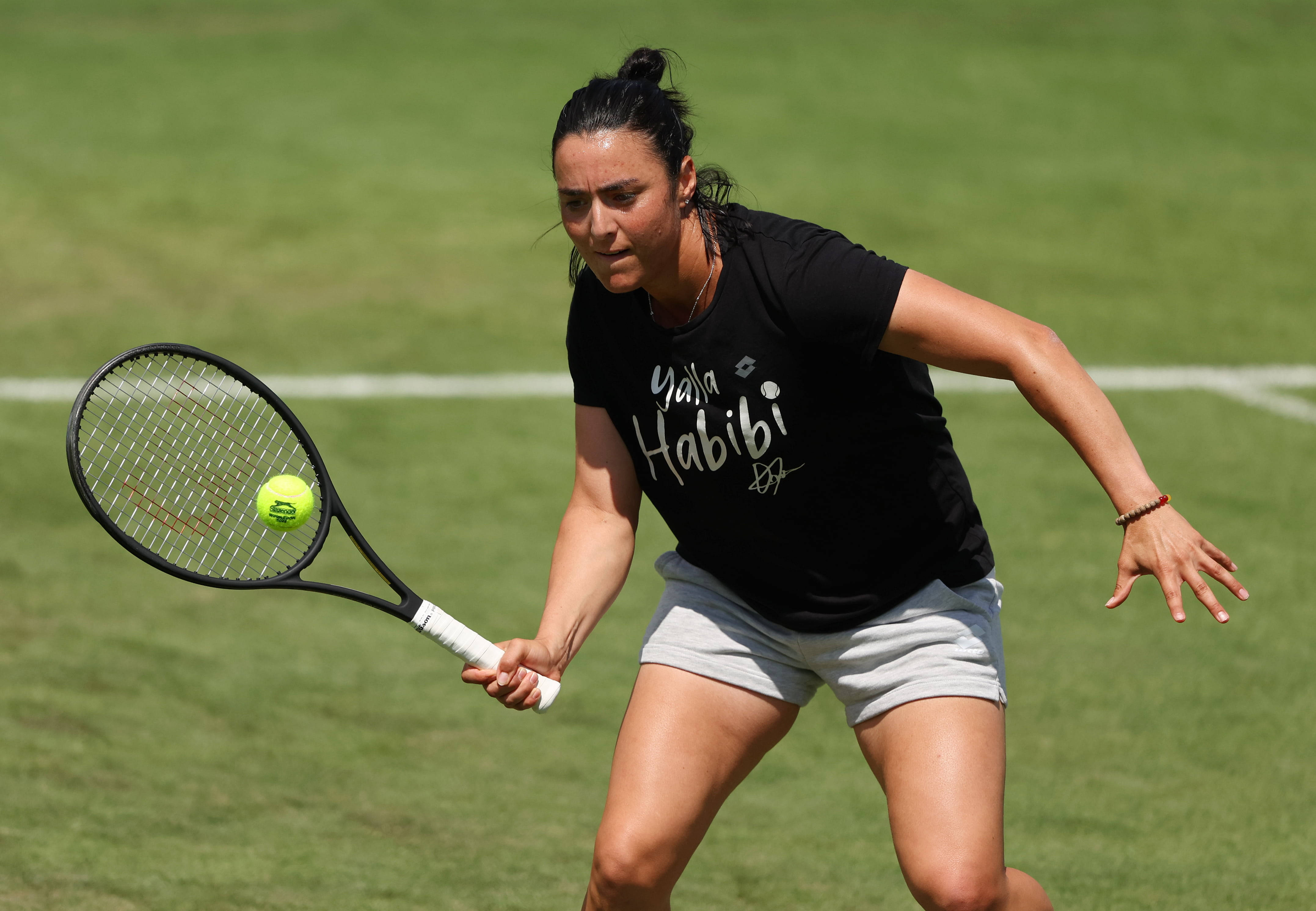 Tennis Ball 桌布 壁紙 — 一位專注的女網球選手在草地場上向前撲出，用球拍擊打一個亮黃色的球。