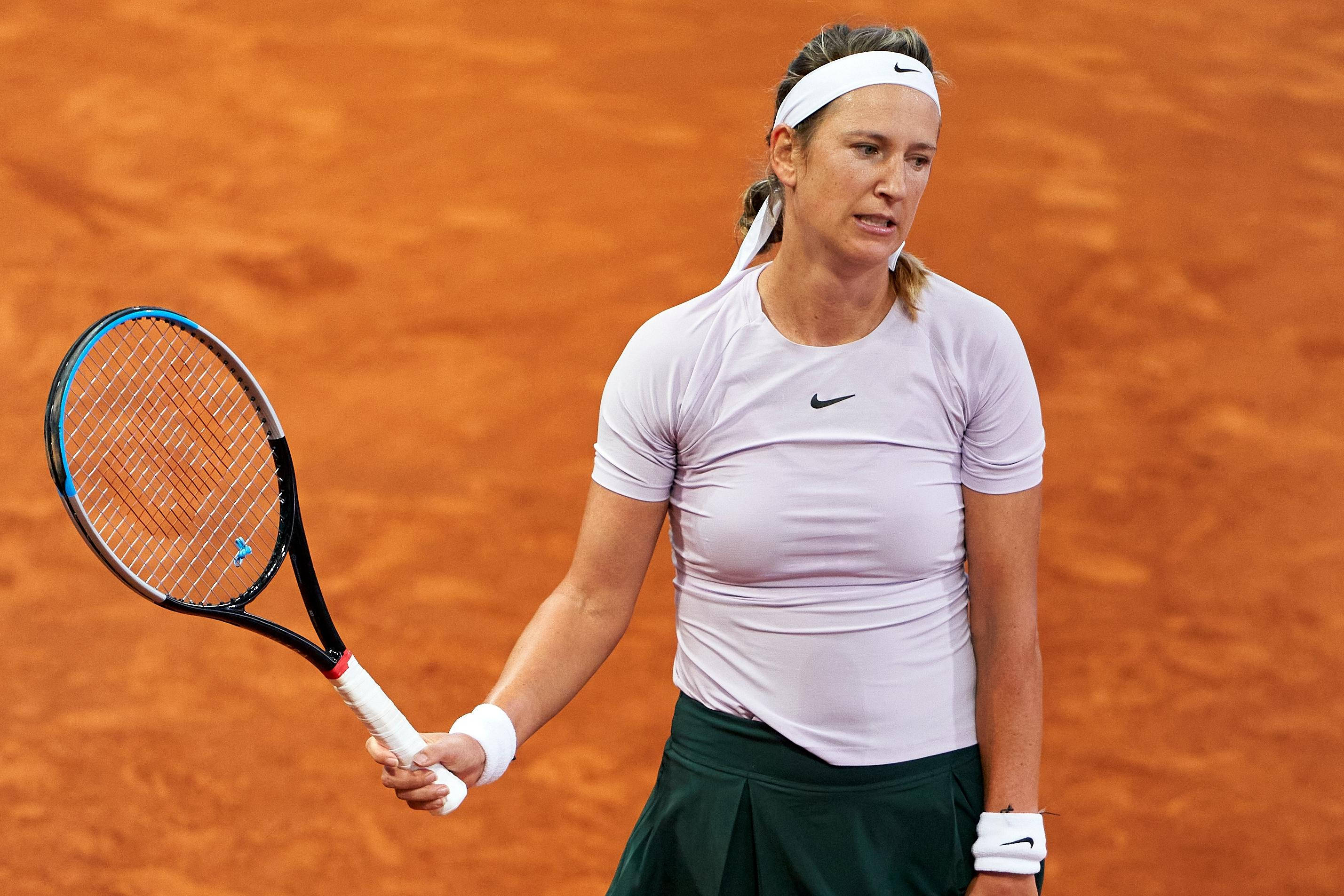 Athletic 桌布 壁紙 — 一位專注的女網球選手在鮮豔的橙色紅土球場上握緊球拍，在明亮的日光下。