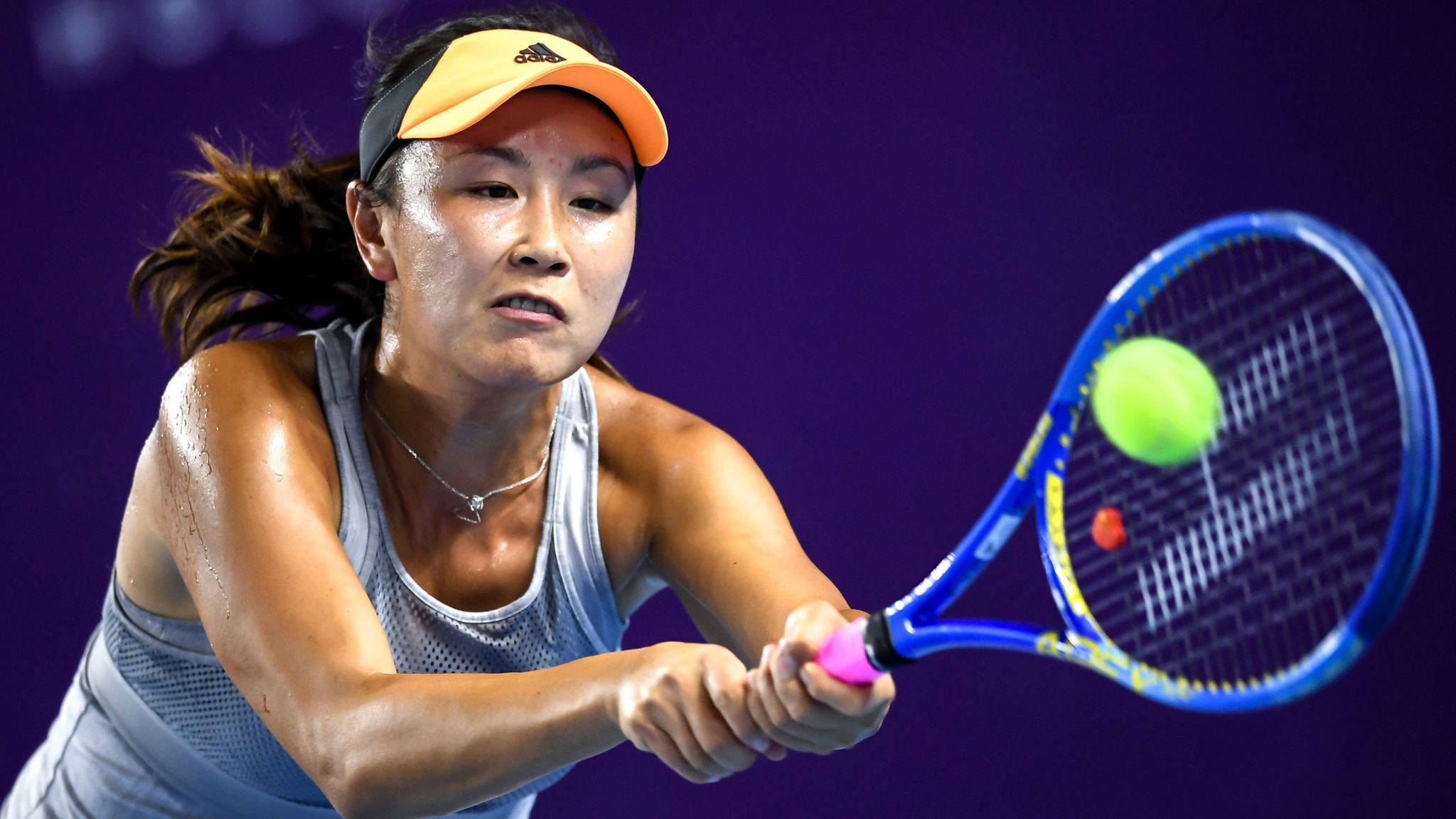 運動 桌布 壁紙 — 一位專注的女網球選手揮動她的藍色球拍，在深紫色背景下擊打一個亮綠色的球。