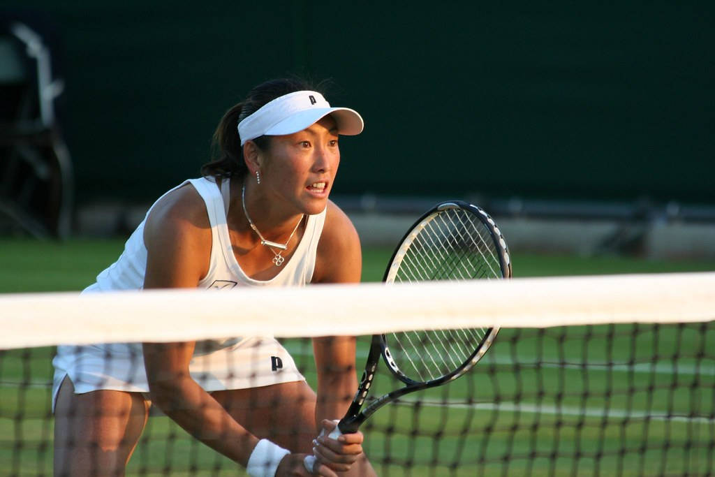 Tennis 桌布 壁紙 — 一位專注的女網球選手身穿白色裝備，在比賽中於網前傾身握著球拍。