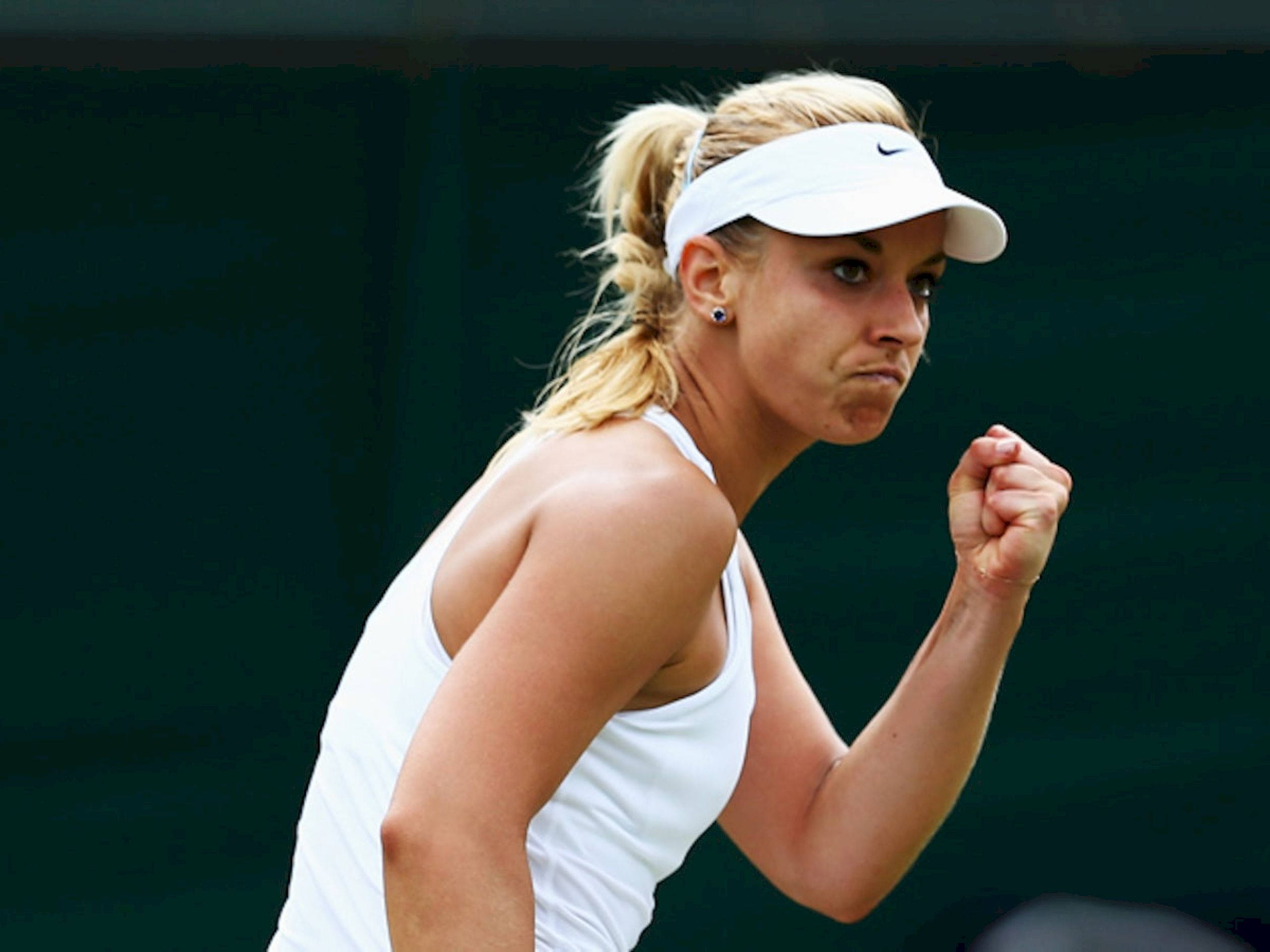 Tennis 桌布 壁紙 — 一位專注的女網球選手身穿白色裝備，在深綠色背景下於比賽中握緊拳頭。